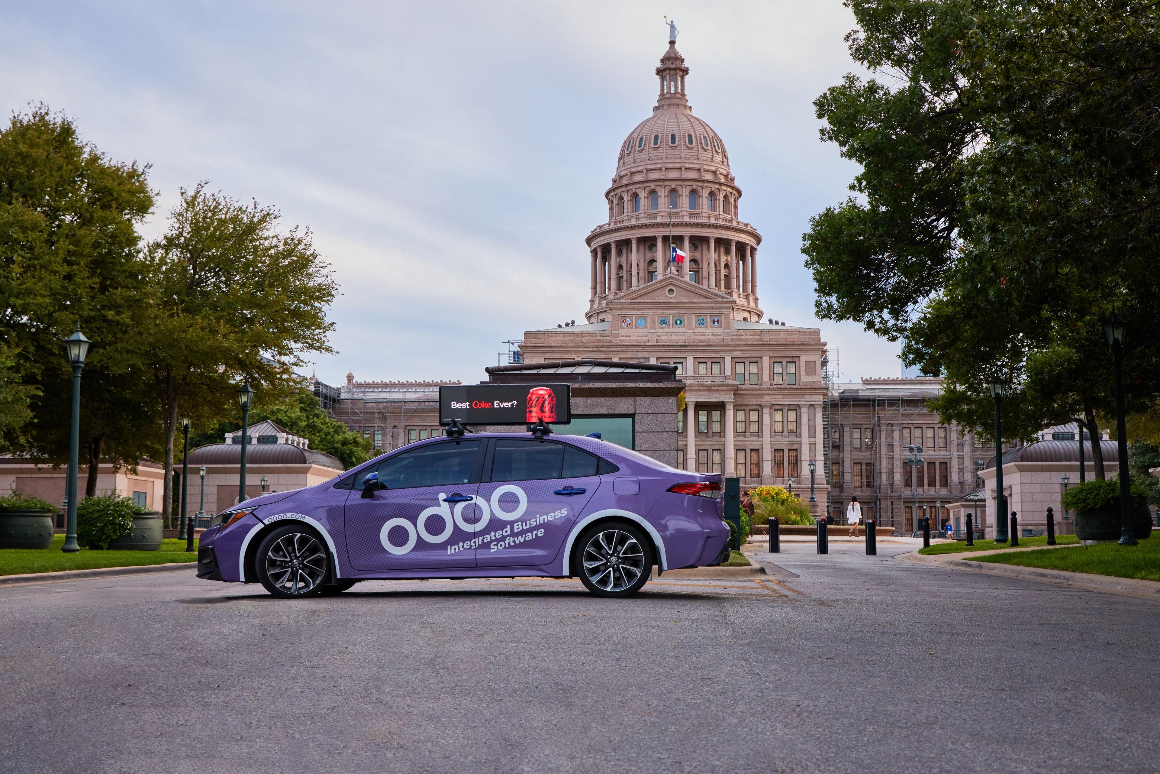 Purple Odoo-branded car with a rooftop digital advertising screen parked — Outdoor media photography, Austin A purple Odoo-branded car with a rooftop digital advertising screen parked in front of the Texas State Capitol at dusk.