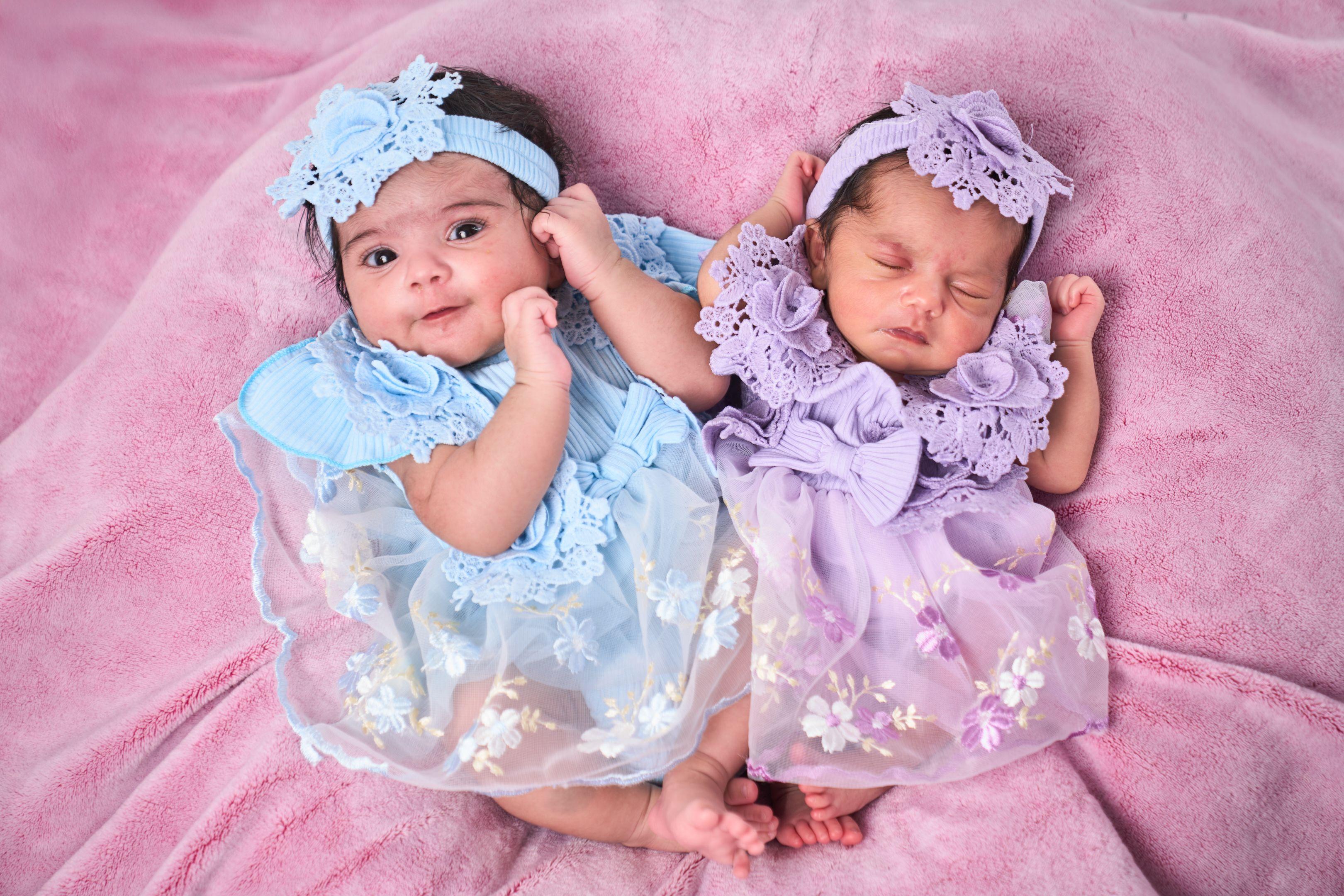 Twin newborns in blue and lilac lace dresses lying side by side — Newborn photography, Austin Twin newborns in blue and lilac lace dresses lying side by side.