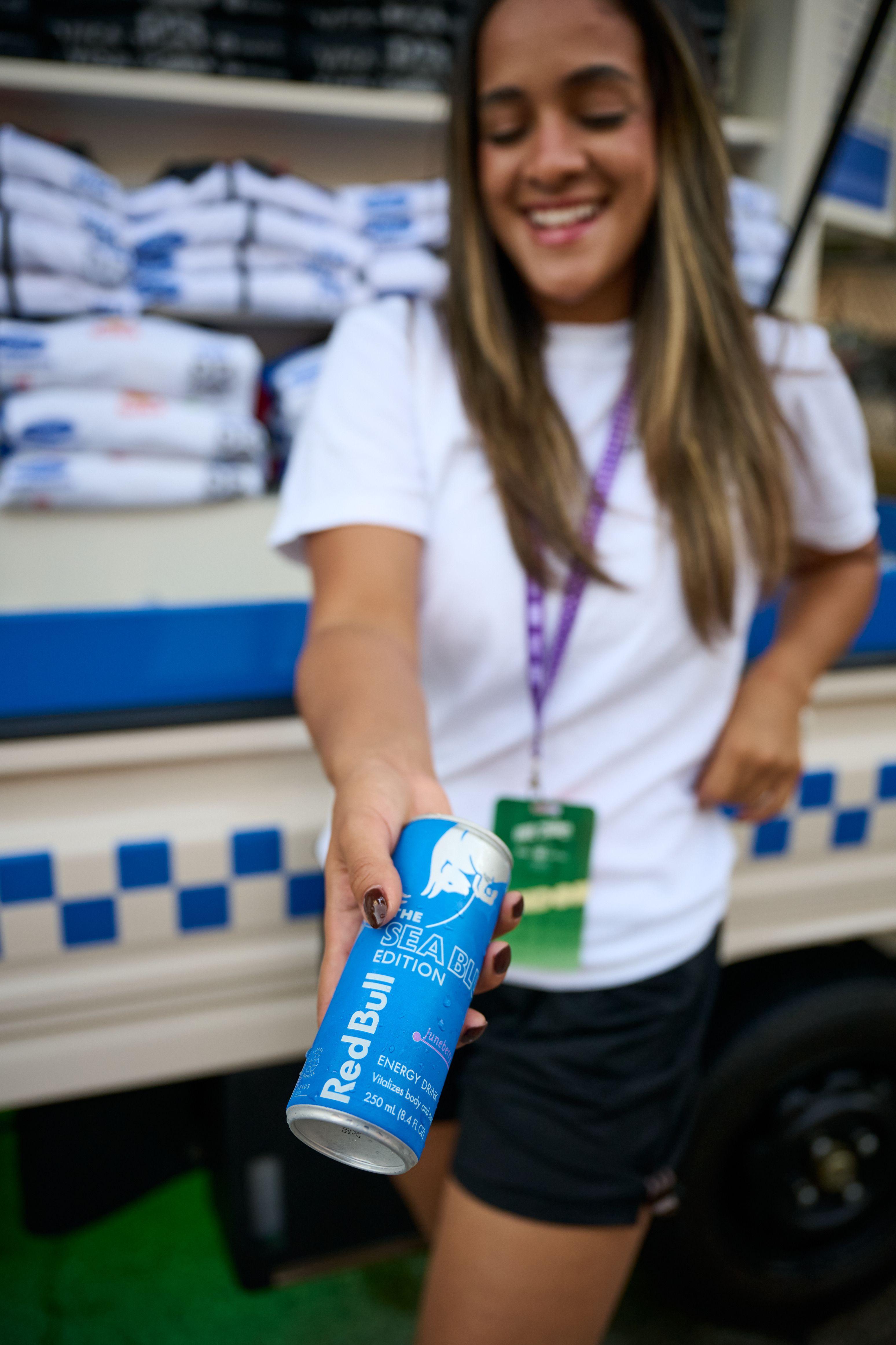 Brand staffer in a white shirt holding out a can of Red Bull beside a branded truck — Brand activation photography, Austin A brand staffer in a white shirt holding out a can of Red Bull beside a branded truck.