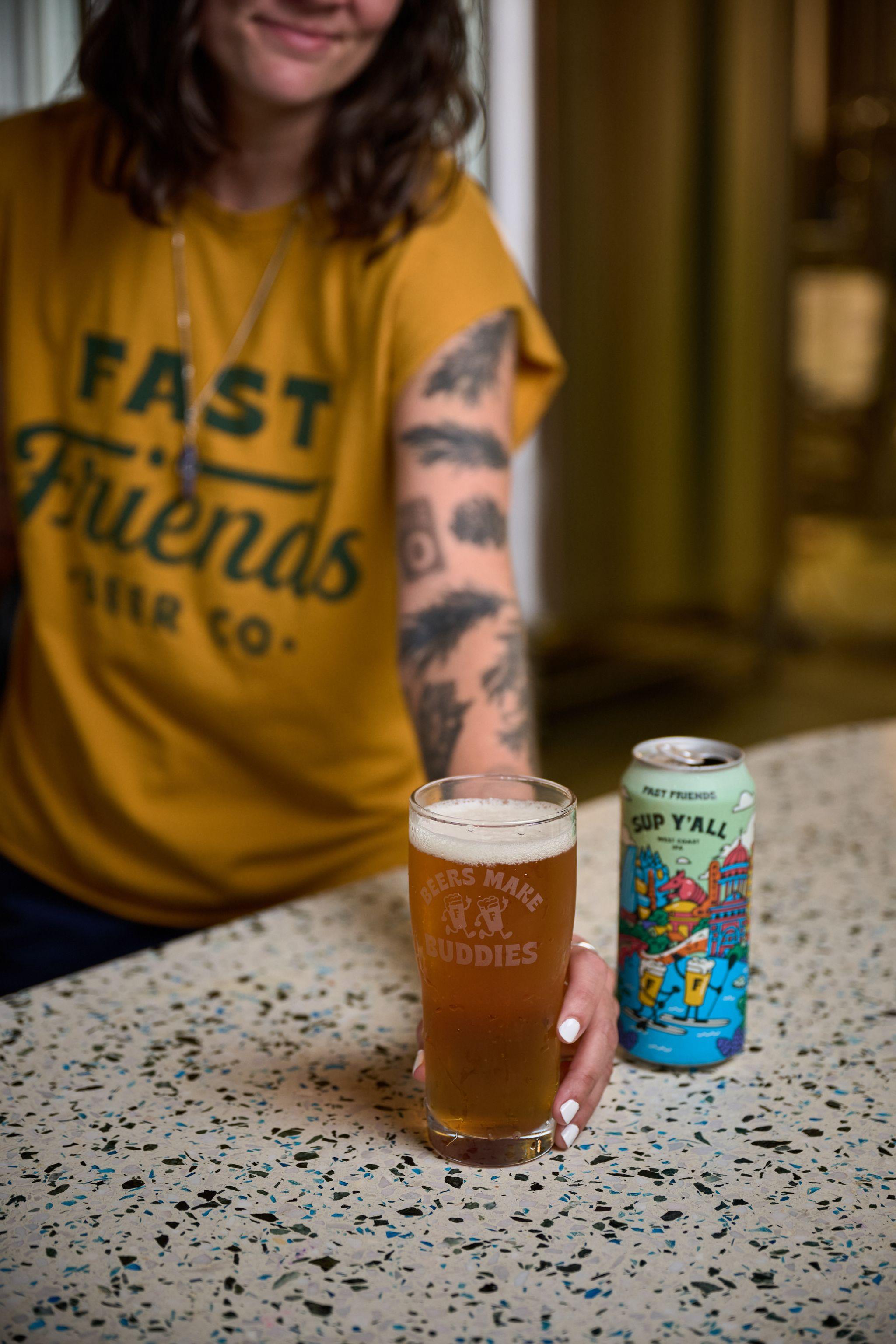 Person in a mustard Fast Friends Beer Co. t-shirt beside a full glass of beer and a printed can — E-commerce & apparel photography, Austin Person in a mustard Fast Friends Beer Co. t-shirt beside a full glass of beer and a printed can on a terrazzo bar