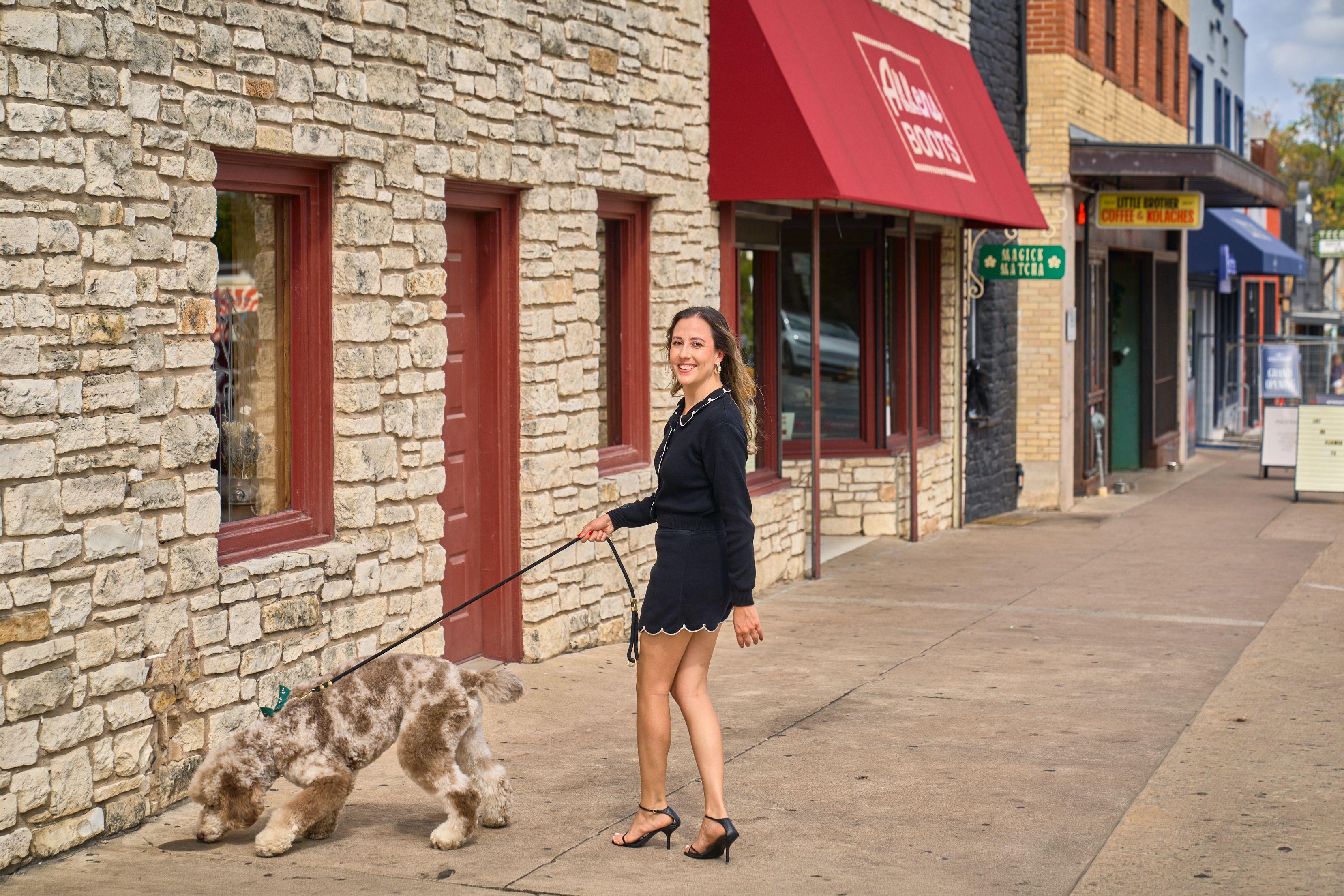 Woman walking her labradoodle past a limestone shopfront with a red awning — South Congress (SoCo) photography, Austin A woman walking her labradoodle past a limestone shopfront with a red awning.