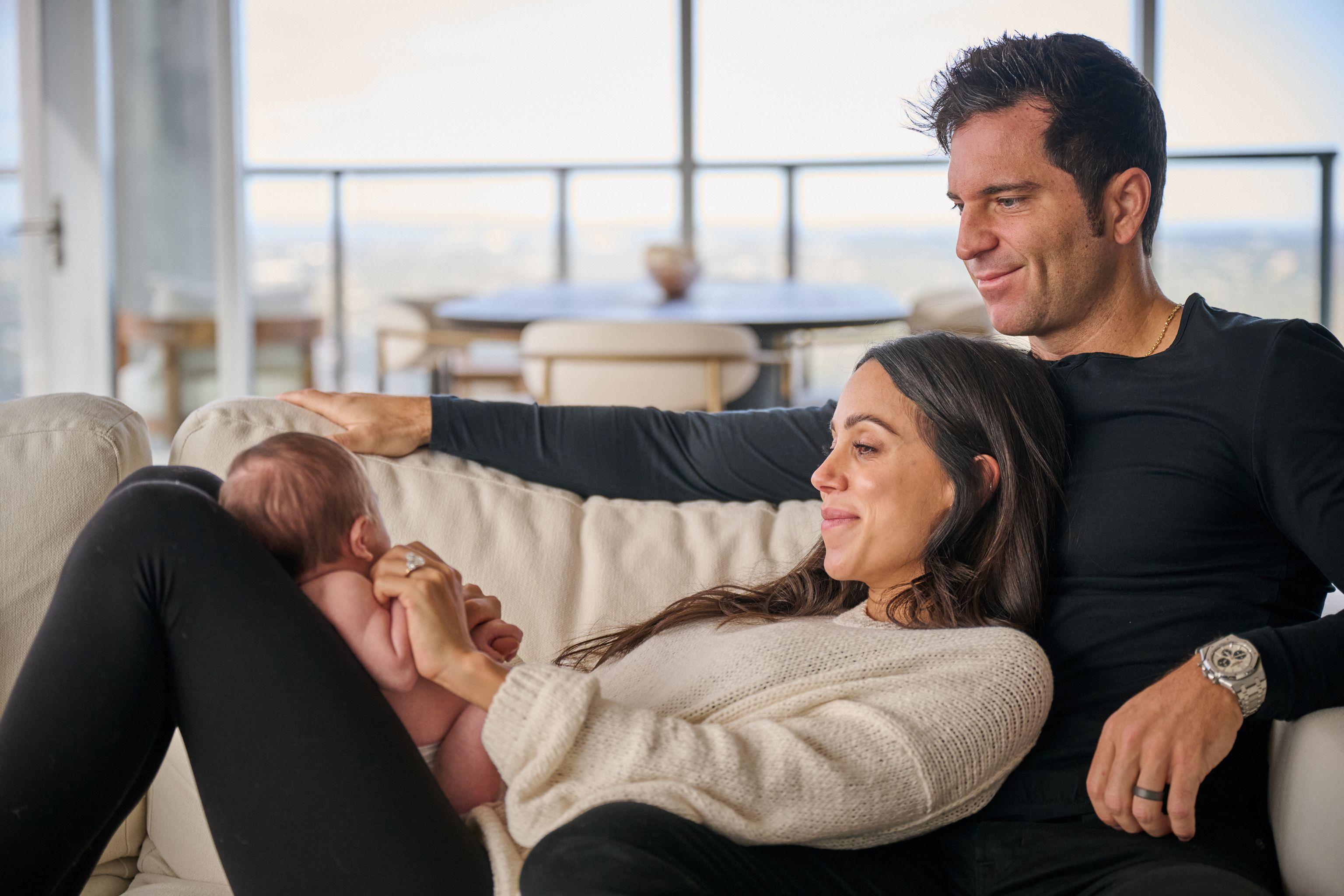Mother reclining with her newborn while the father leans over them, city windows — Newborn photography, Austin A mother reclining with her newborn while the father leans over them, city windows behind.