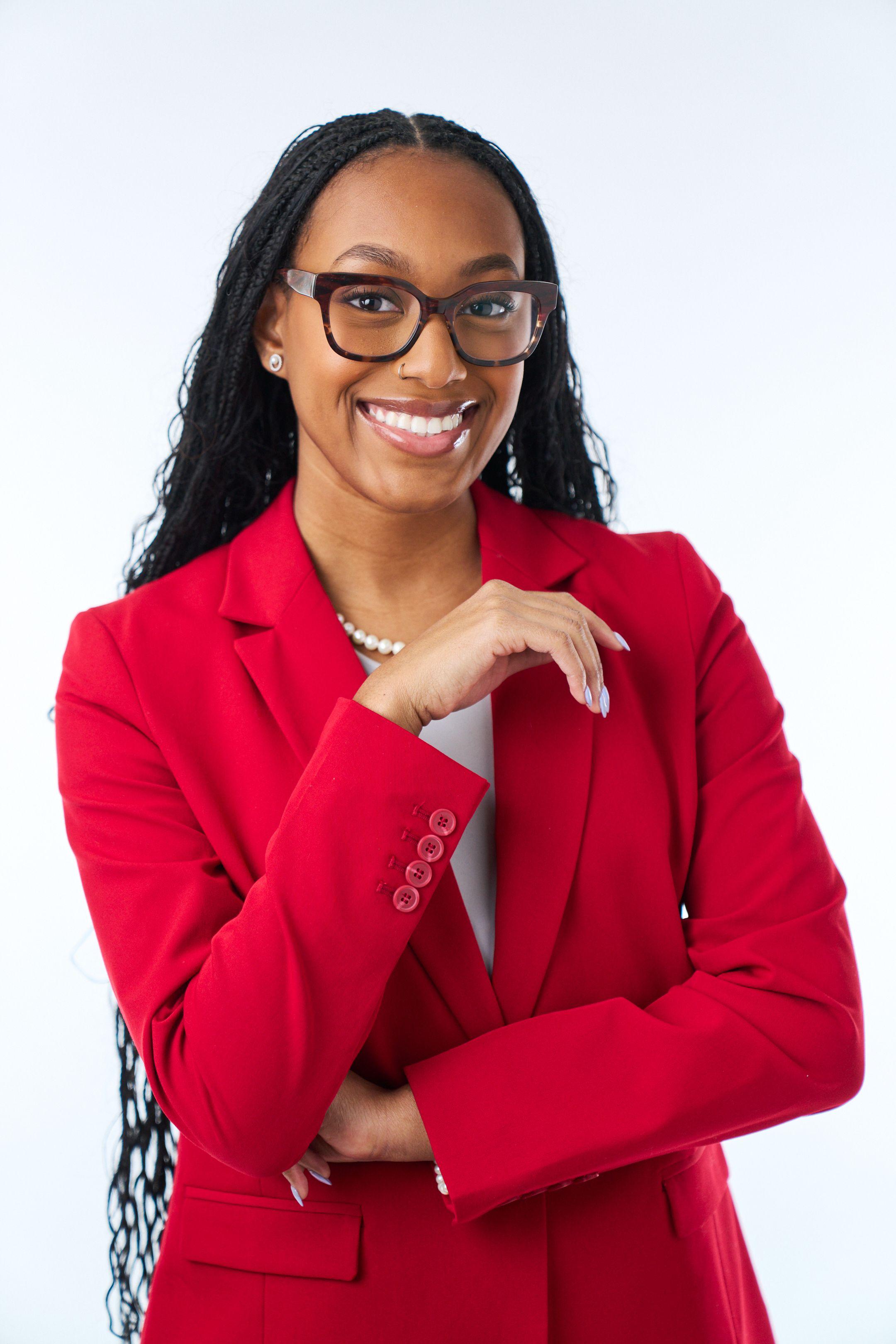 Woman in a red blazer and glasses smiling with her arms folded against a white backdrop — Headshot photography, Austin A woman in a red blazer and glasses smiling with her arms folded against a white backdrop.