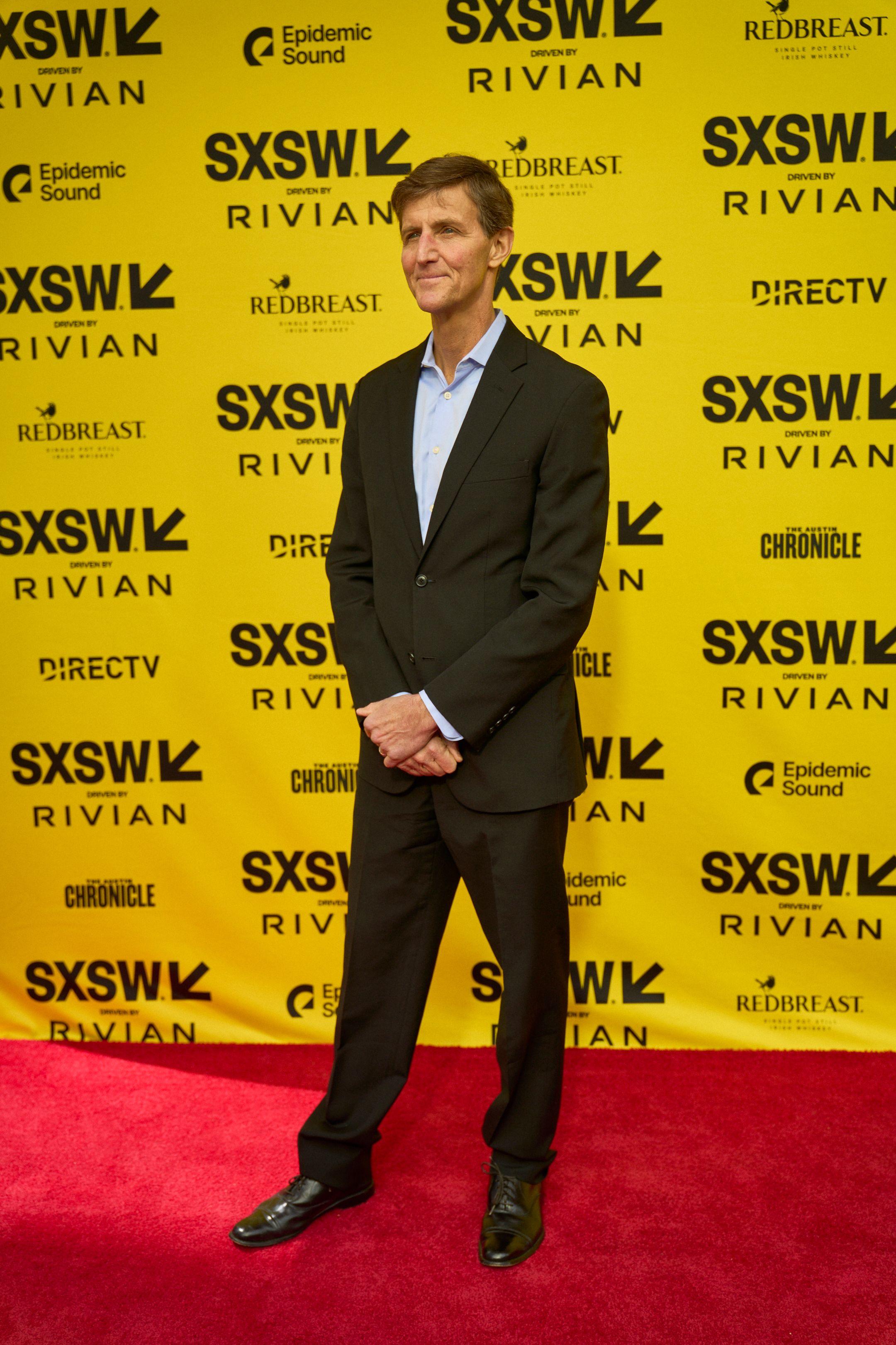 Man in a dark suit standing on a red carpet in front of a yellow SXSW step-and-repeat — Production behind-the-scenes, Austin Man in a dark suit standing on a red carpet in front of a yellow SXSW step-and-repeat
