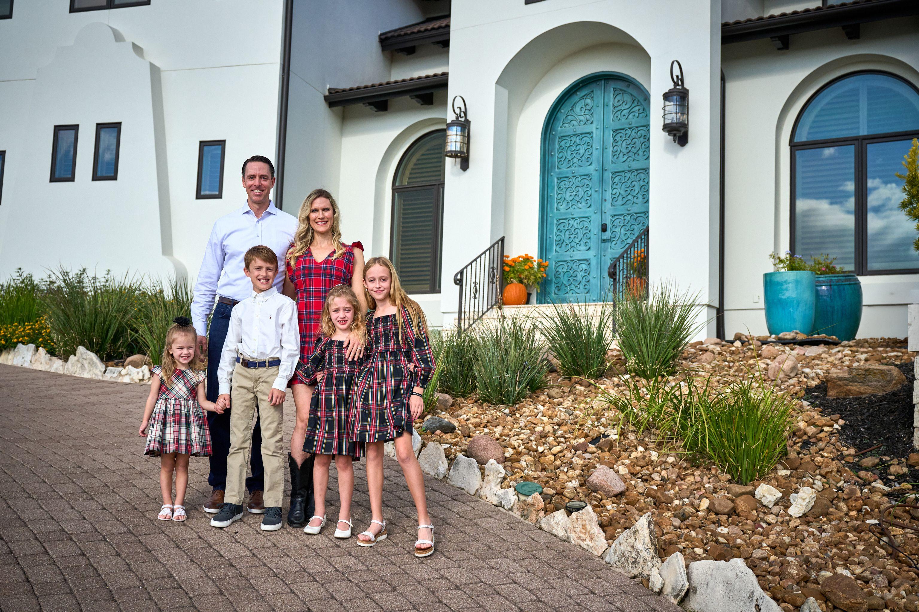 Family in tartan and red posed on the drive in front of a Spanish-style house — Family Portraits photography, Austin A family in tartan and red posed on the drive in front of a Spanish-style house.