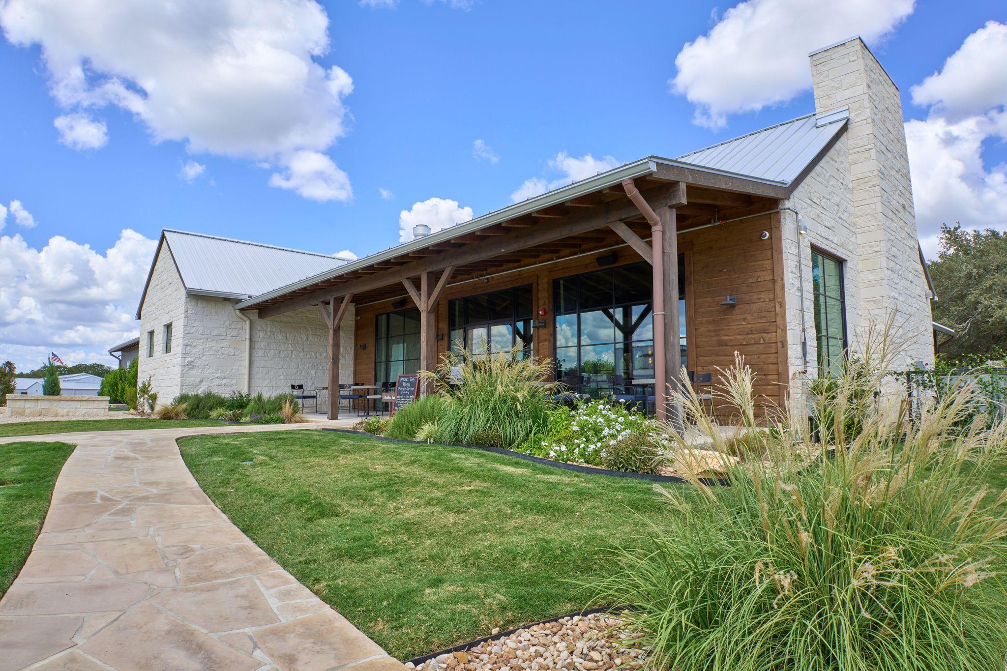 Low timber-framed building with a covered porch and landscaped lawn — Architectural photography, Austin A low timber-framed building with a covered porch and landscaped lawn.
