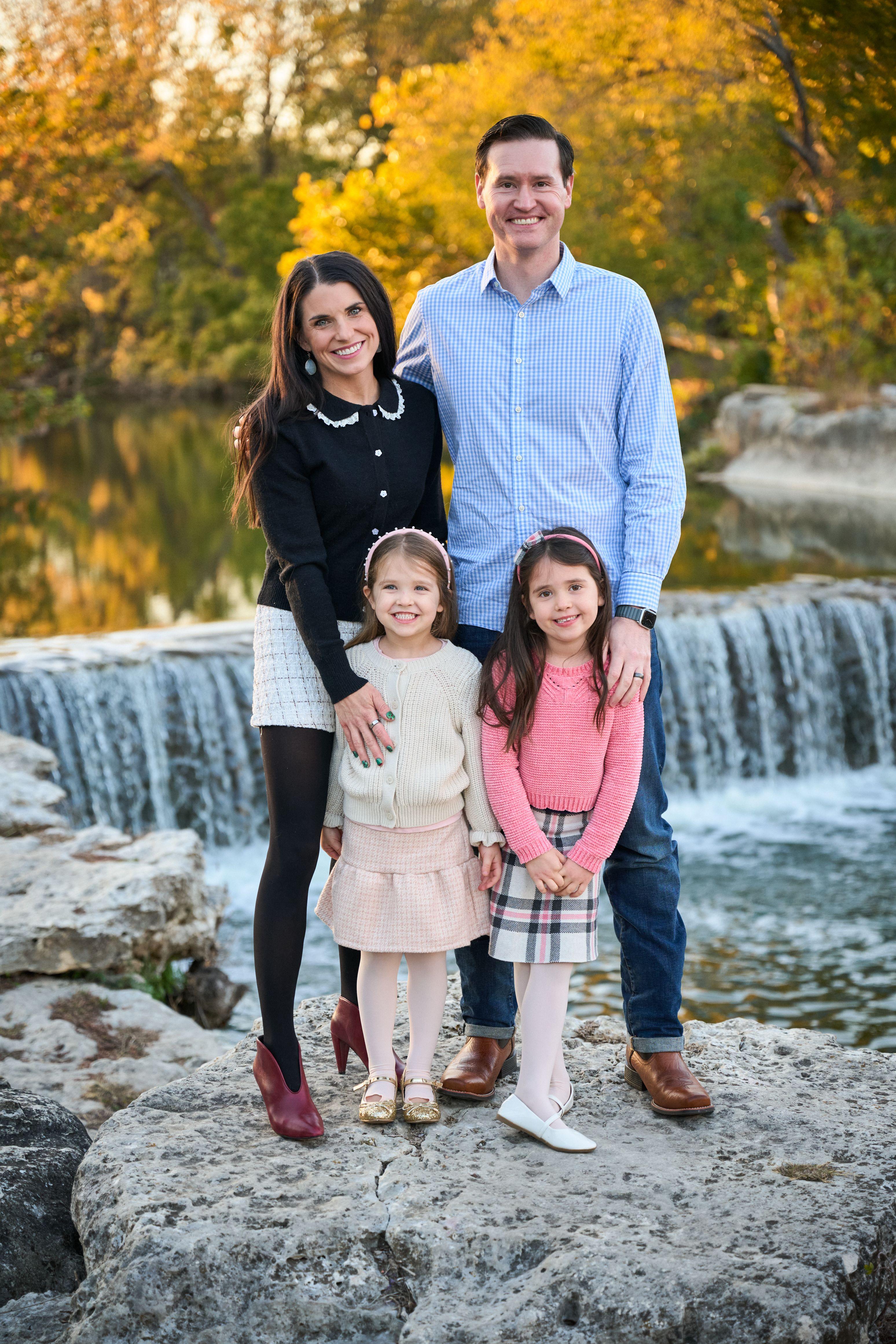 Family of four standing on rocks in front of a wide waterfall in autumn — Family Portraits photography, Austin A family of four standing on rocks in front of a wide waterfall in autumn.