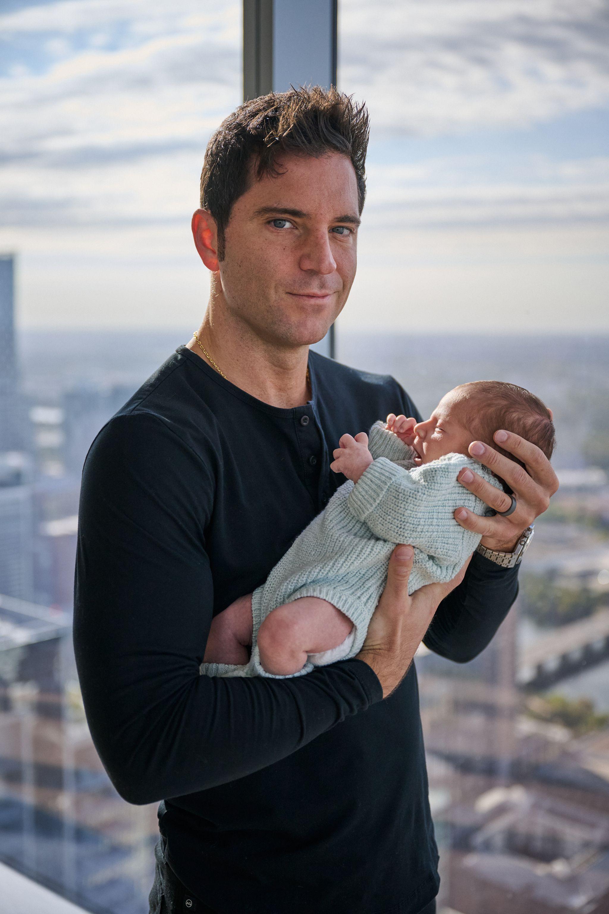 Father holding his newborn up in both hands in front of a high-rise window at dusk — Newborn photography, Austin A father holding his newborn up in both hands in front of a high-rise window at dusk.