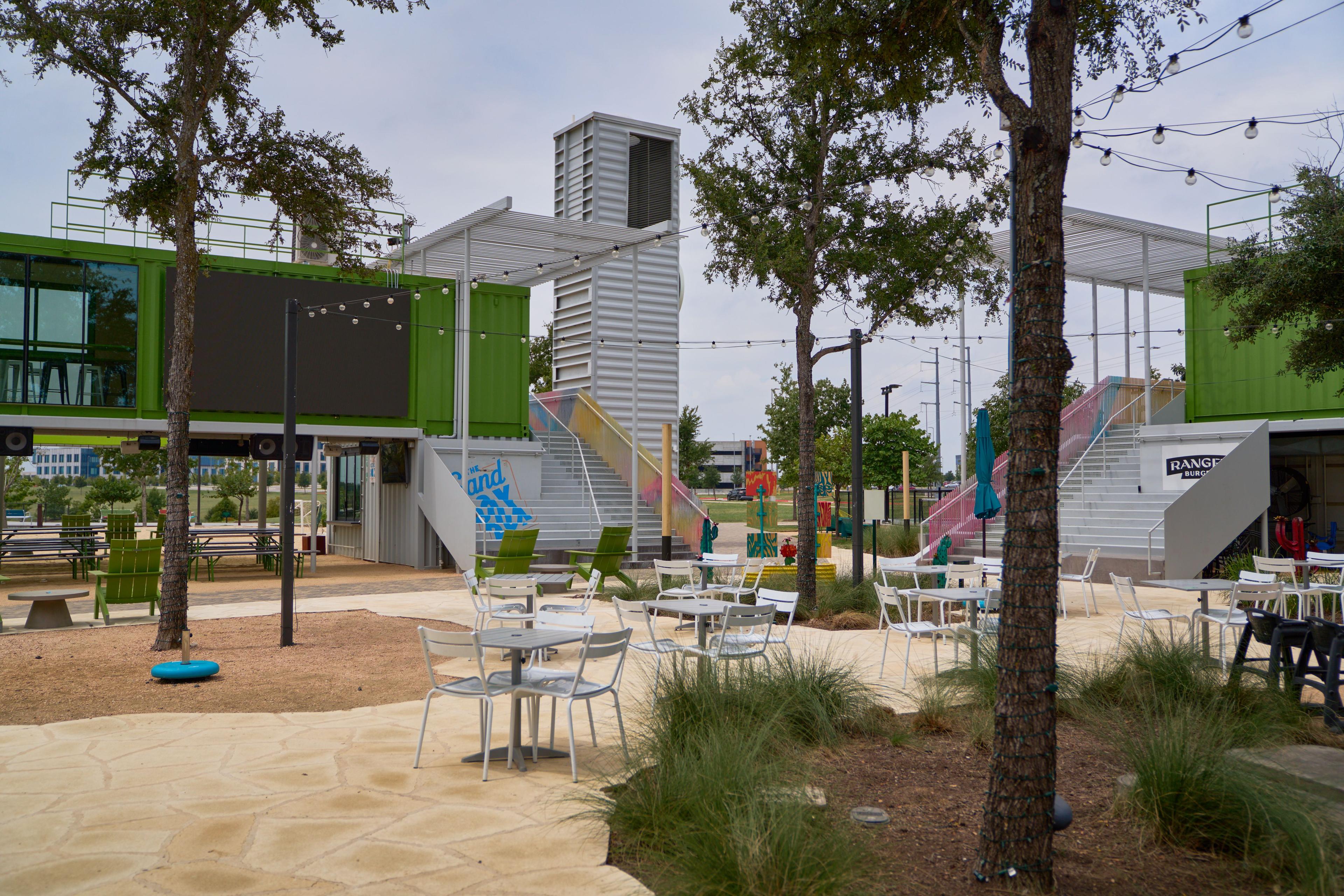 Outdoor patio with cafe tables beside a container village — Hospitality & leisure photography, Austin An outdoor patio with cafe tables beside a container village.