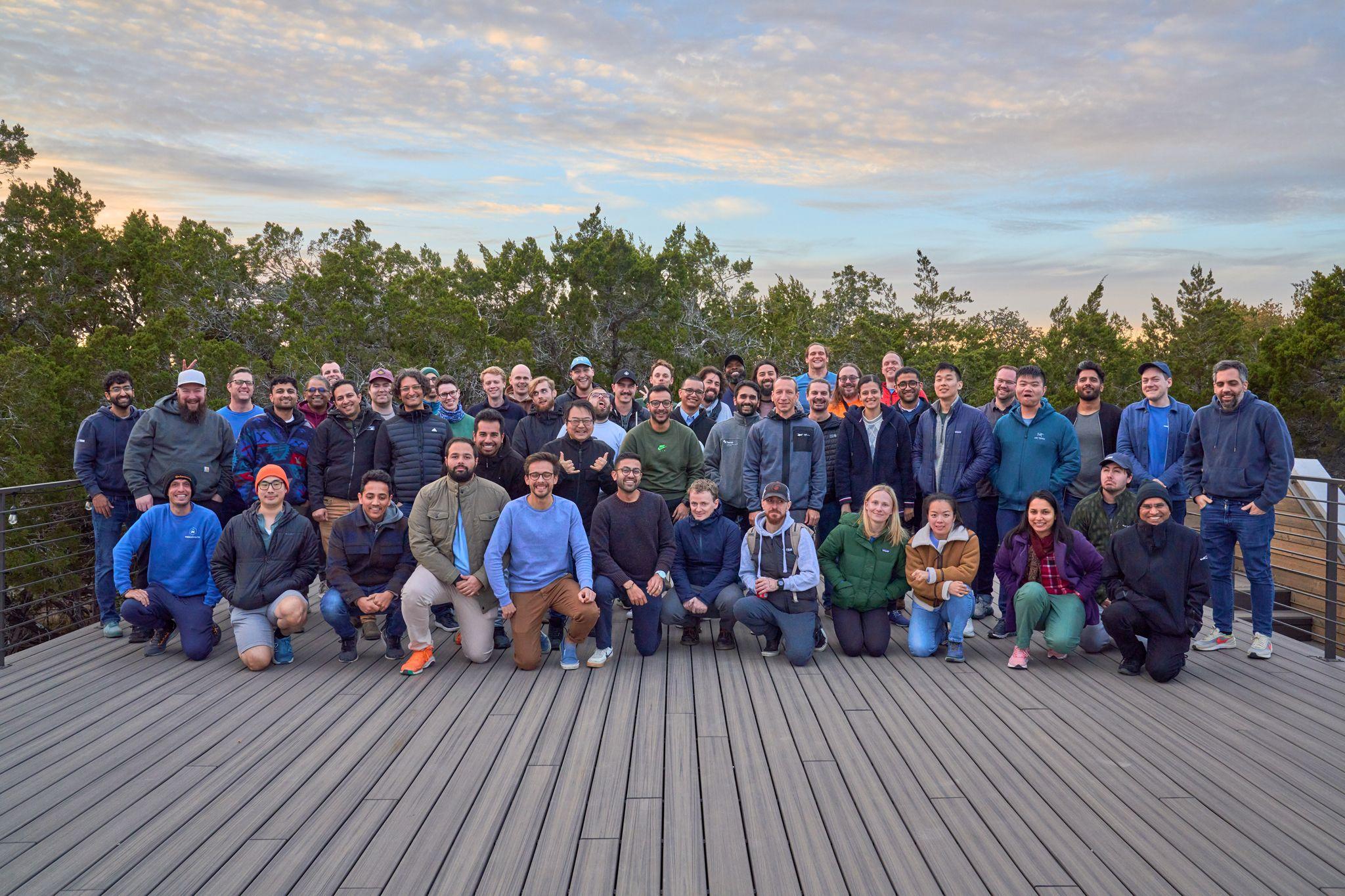 Large group seated and standing together on a wooden deck with trees — Team offsite photography, Austin Large group seated and standing together on a wooden deck with trees behind