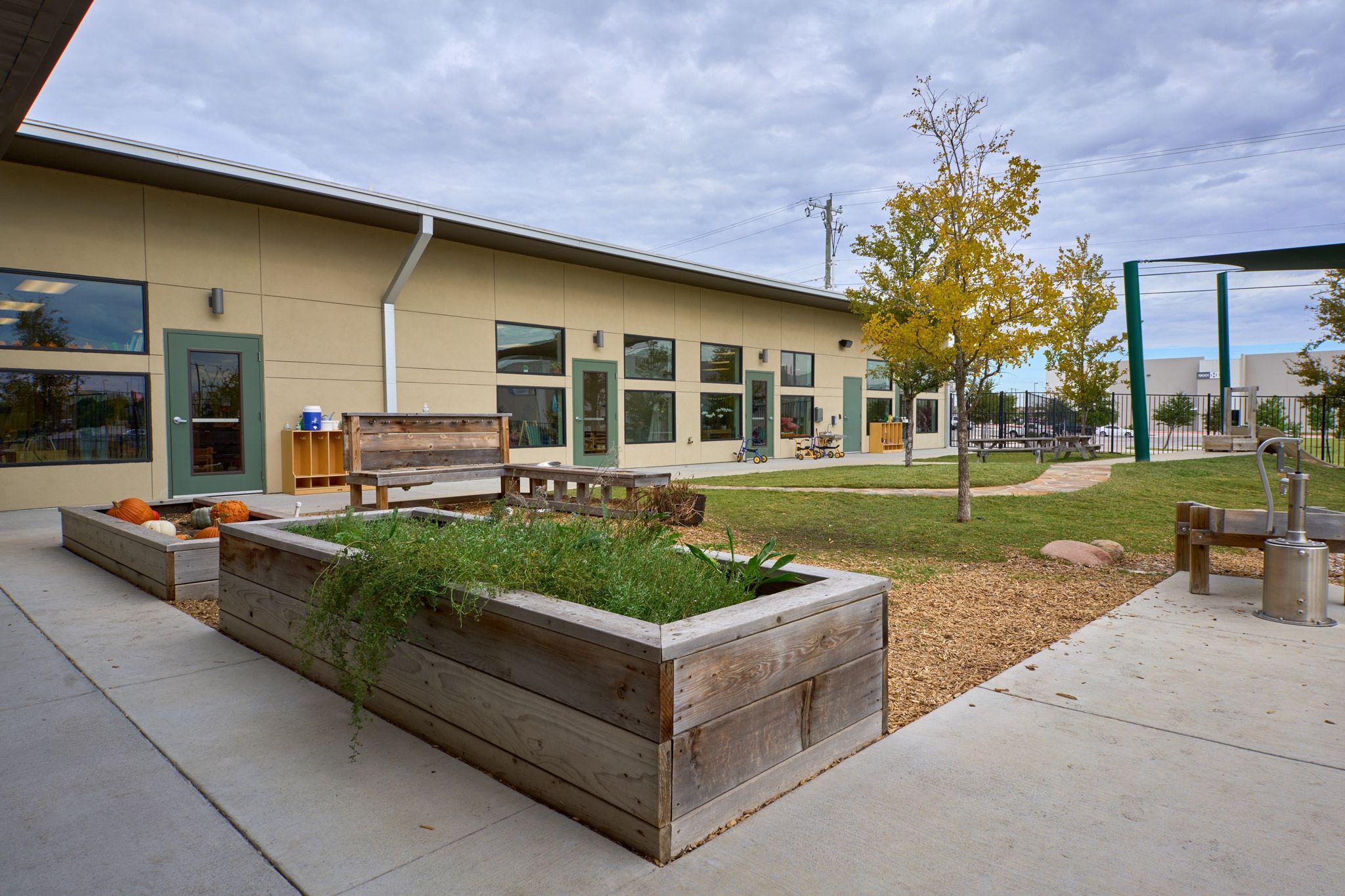 School building exterior with a raised timber planter bed and young trees — School event photography, Austin School building exterior with a raised timber planter bed and young trees