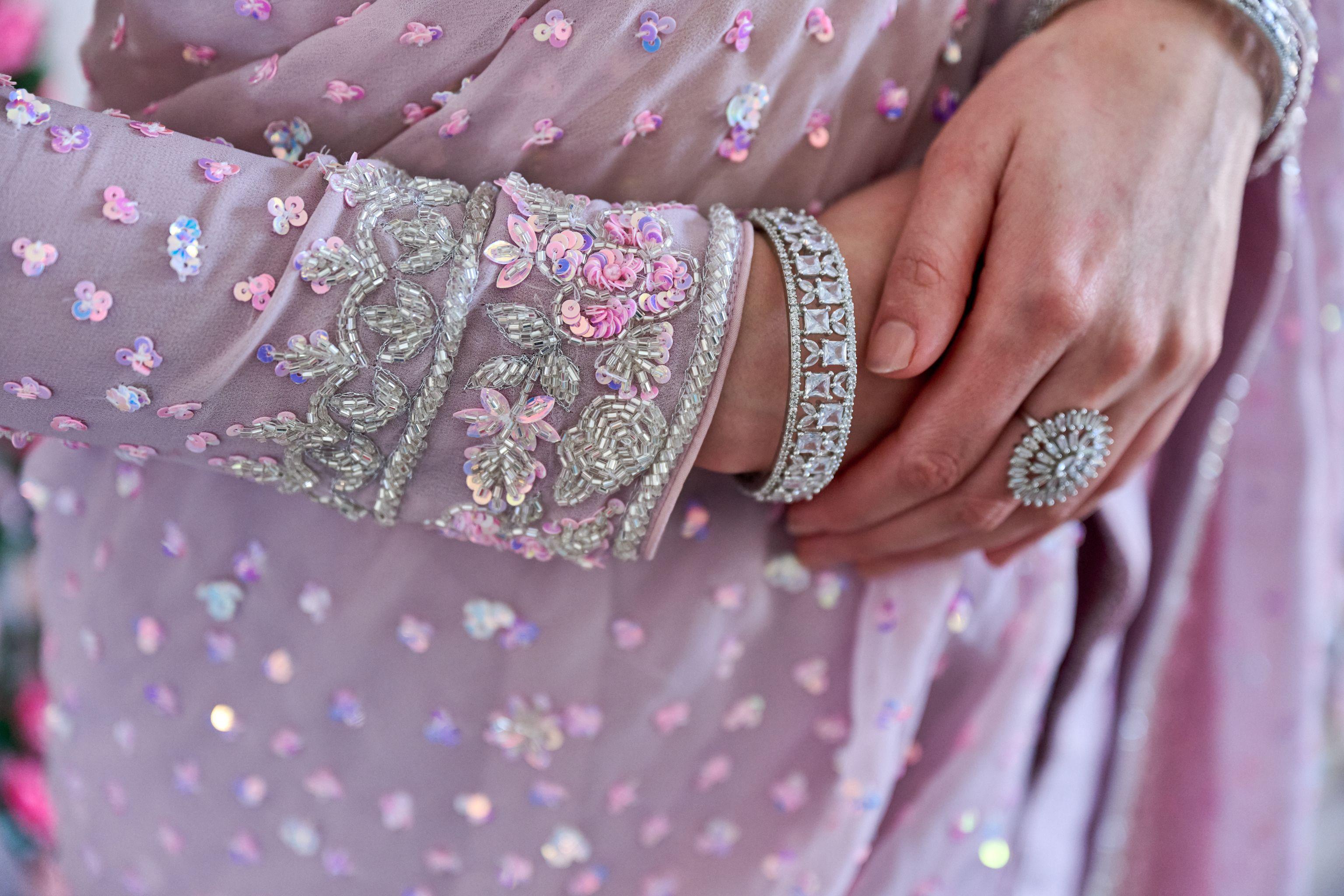 Close detail of an embroidered pink lehenga sleeve and bangles against the groom's hand — Weddings photography, Austin A close detail of an embroidered pink lehenga sleeve and bangles against the groom's hand.