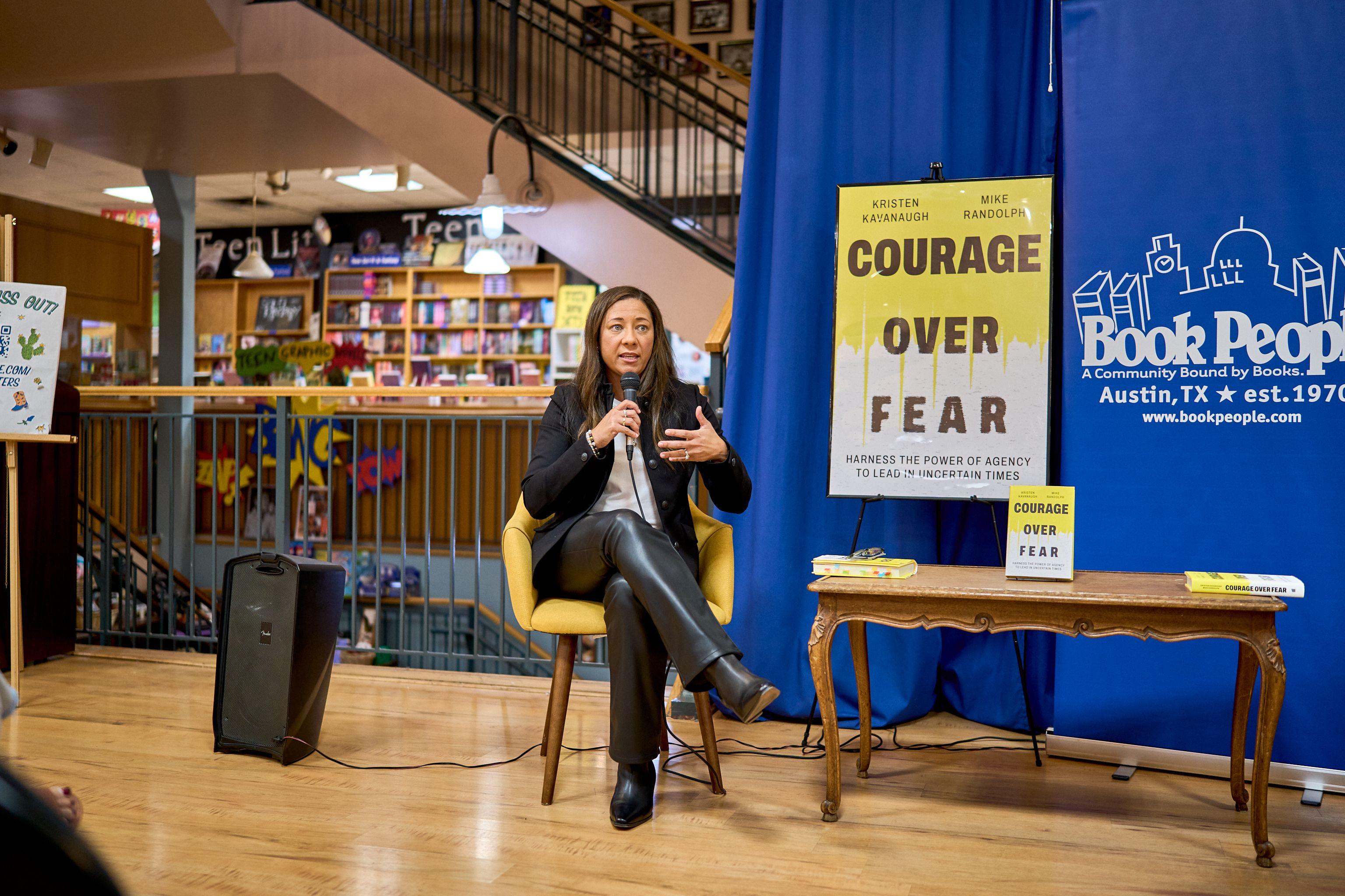 Speaker seated on stage beside a Courage Over Fear book banner — Brand activation photography, Austin A speaker seated on stage beside a Courage Over Fear book banner.