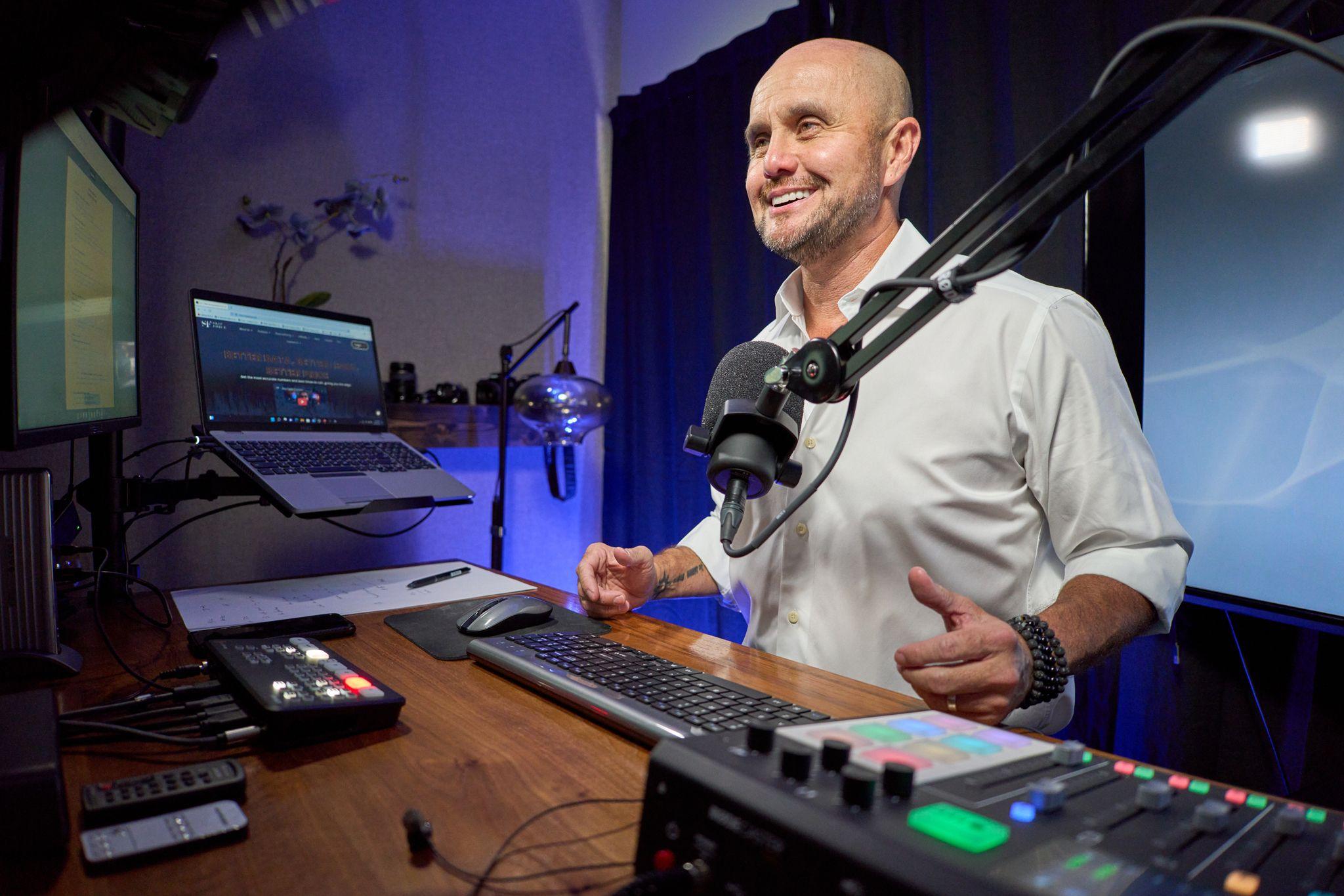 Presenter at a microphone in a studio with monitors and a control surface on the desk — Production behind-the-scenes, Austin Presenter at a microphone in a studio with monitors and a control surface on the desk
