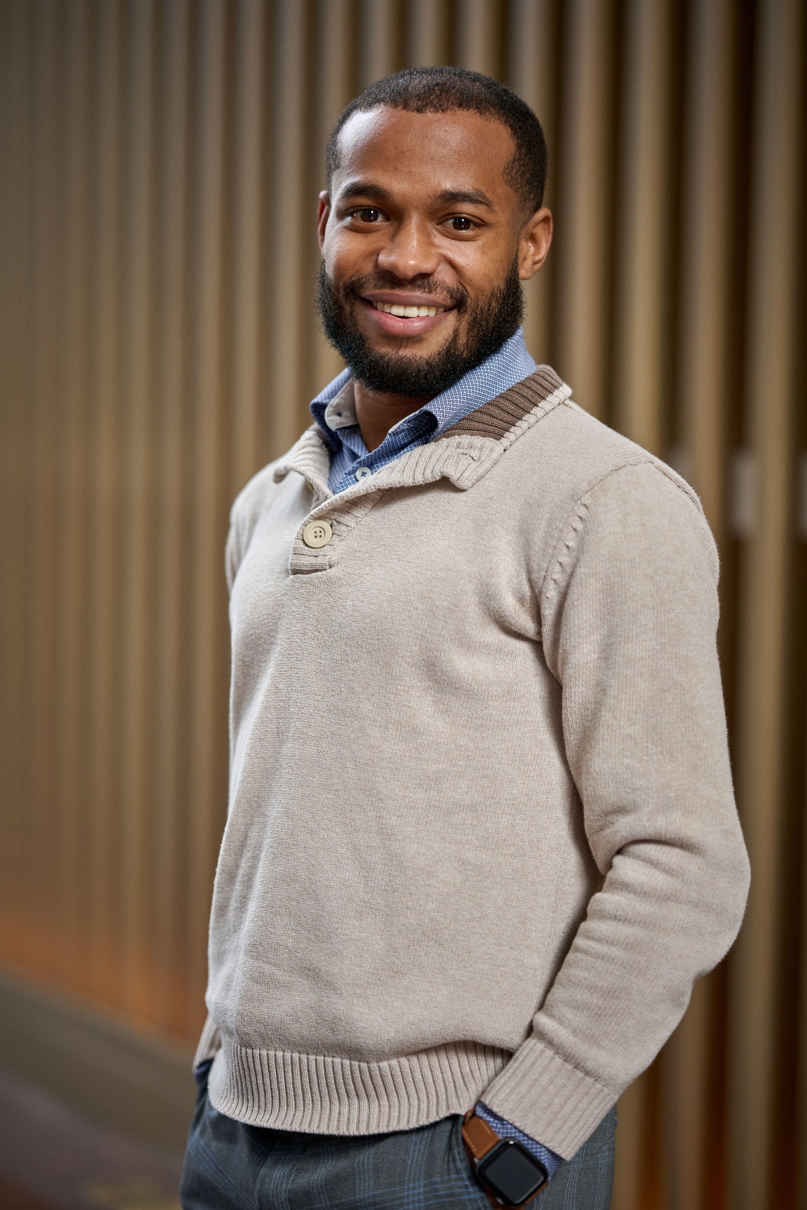 Man in a cream sweater smiling in front of a slatted wood wall — Headshot photography, Austin A man in a cream sweater smiling in front of a slatted wood wall.