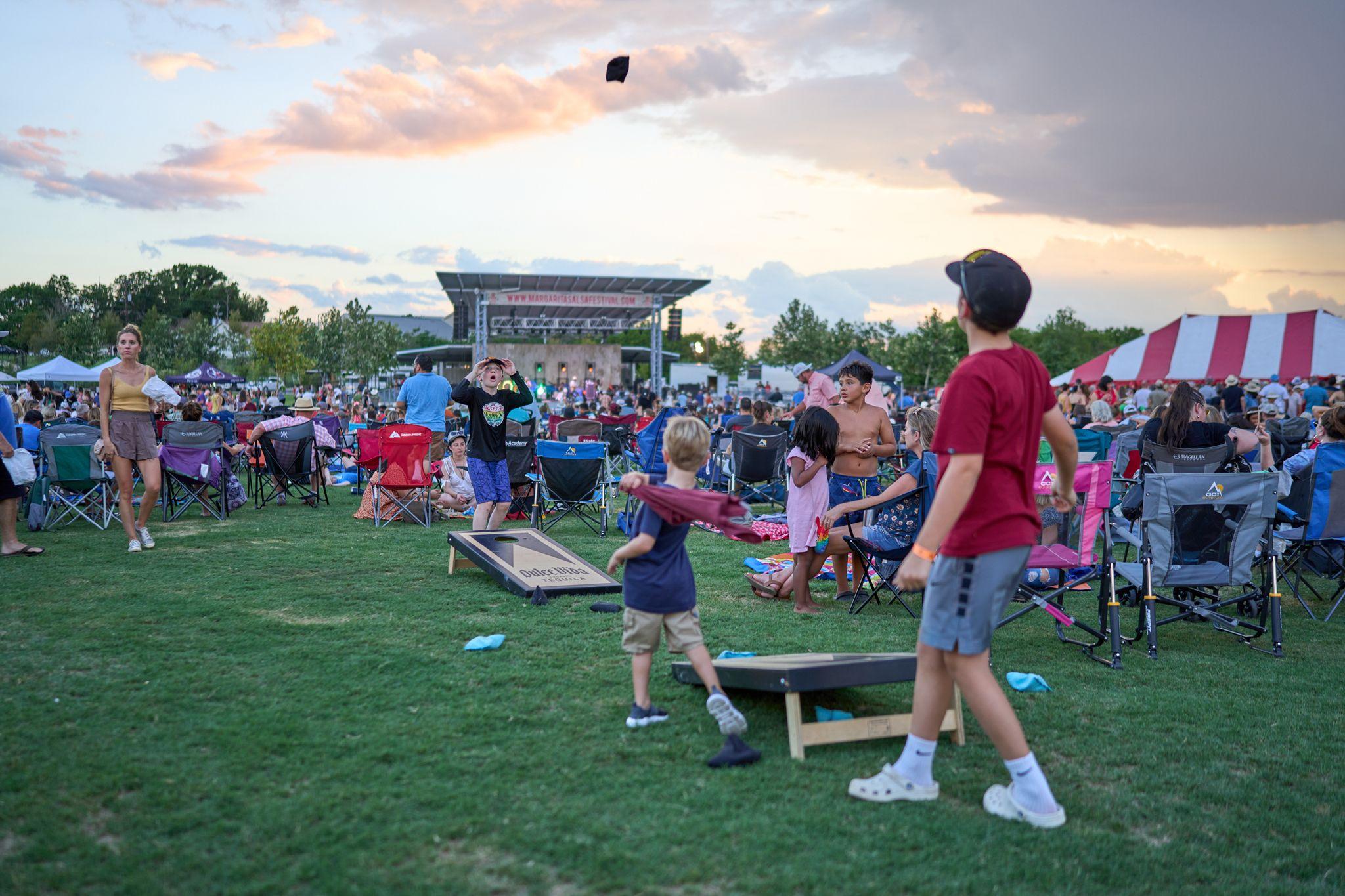 Families playing cornhole on the lawn in front of a festival stage at sunset — Festival photography, Austin Families playing cornhole on the lawn in front of a festival stage at sunset.