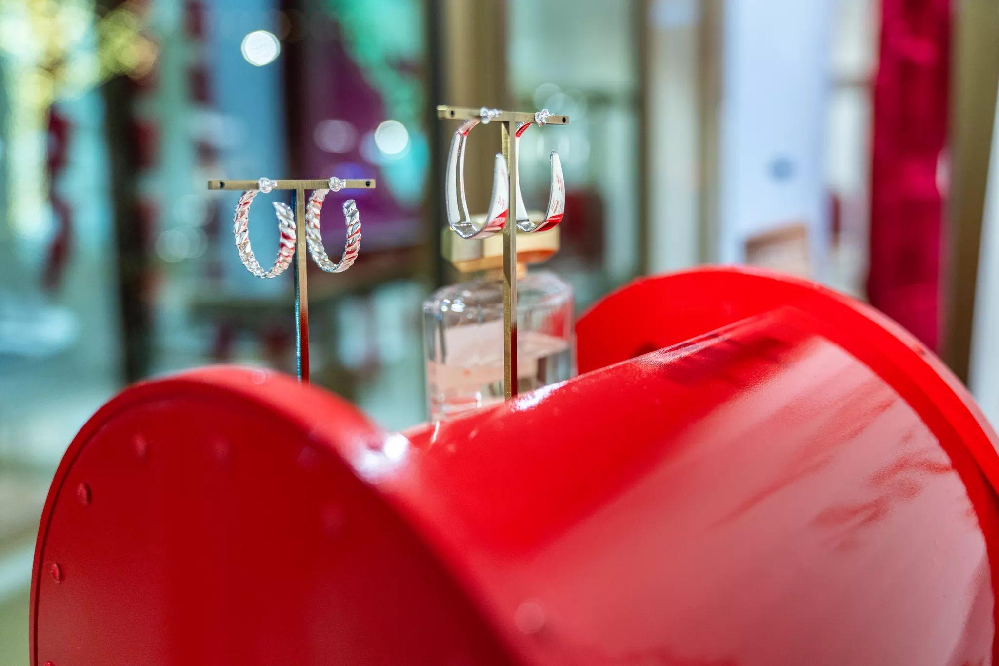 Gold hoop earrings on a display stand behind a glossy red retail fixture — E-commerce & apparel photography, Austin Gold hoop earrings on a display stand behind a glossy red retail fixture