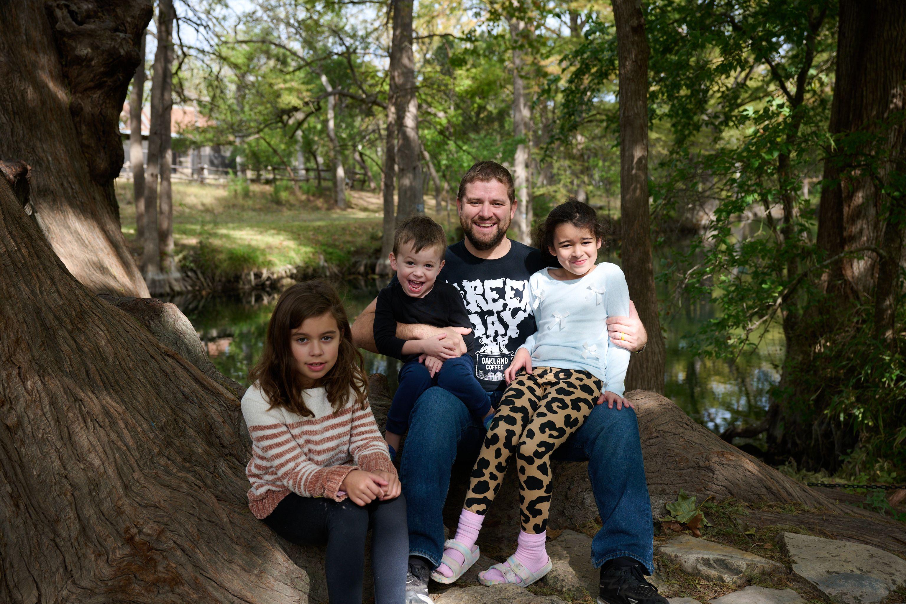 Family sitting together on the rock ledge beside the cypress-lined creek at Wimberley — Wimberley TX photography, Austin A family sitting together on the rock ledge beside the cypress-lined creek at Wimberley