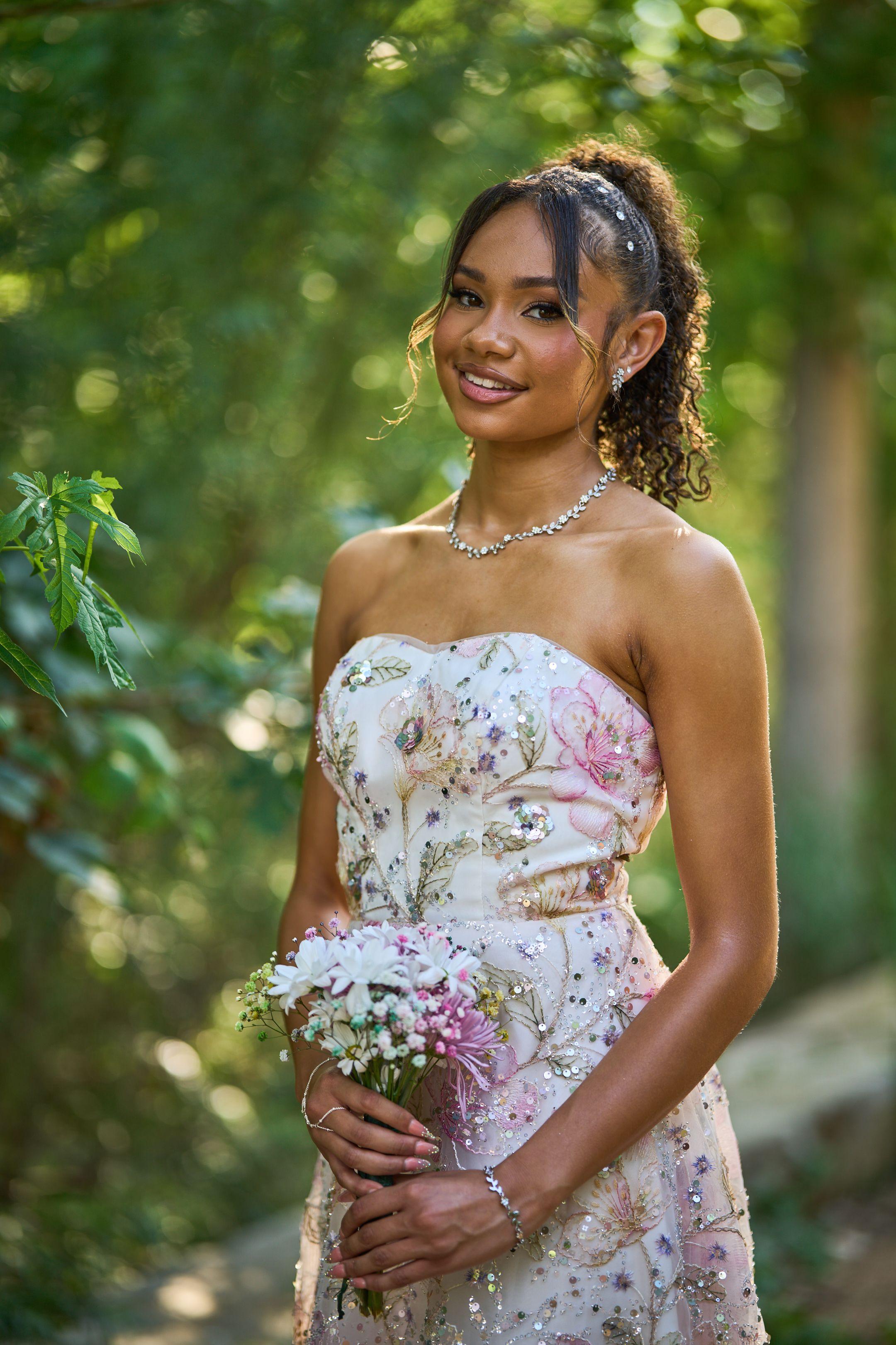 Young woman in an embroidered floral gown holding a bouquet under green trees — Butler Metro Park photography, Austin A young woman in an embroidered floral gown holding a bouquet under green trees.