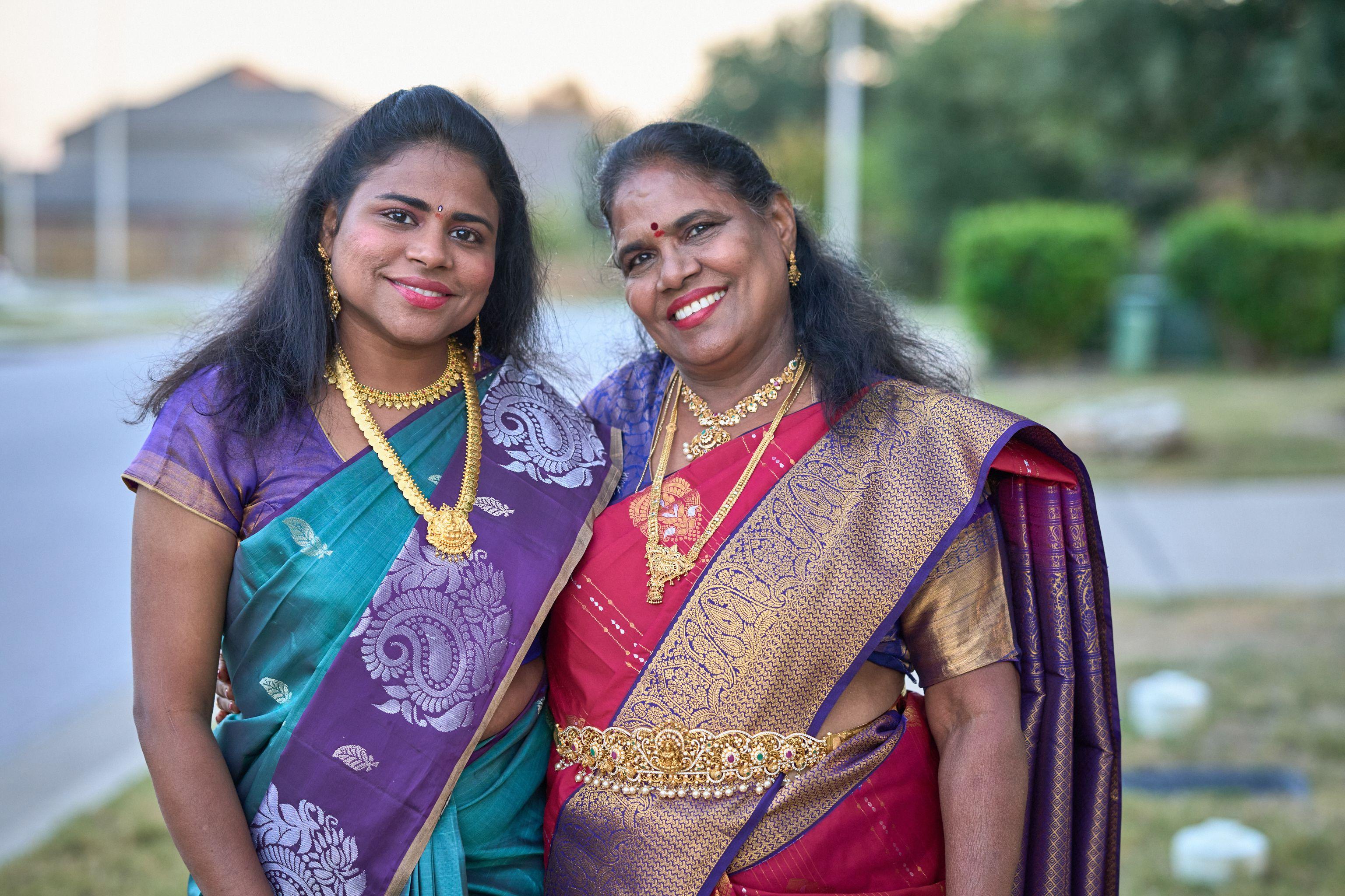 Two women in richly colored silk saris and gold jewelry smiling together outdoors — Religious Ceremonies photography, Austin Two women in richly colored silk saris and gold jewelry smiling together outdoors.