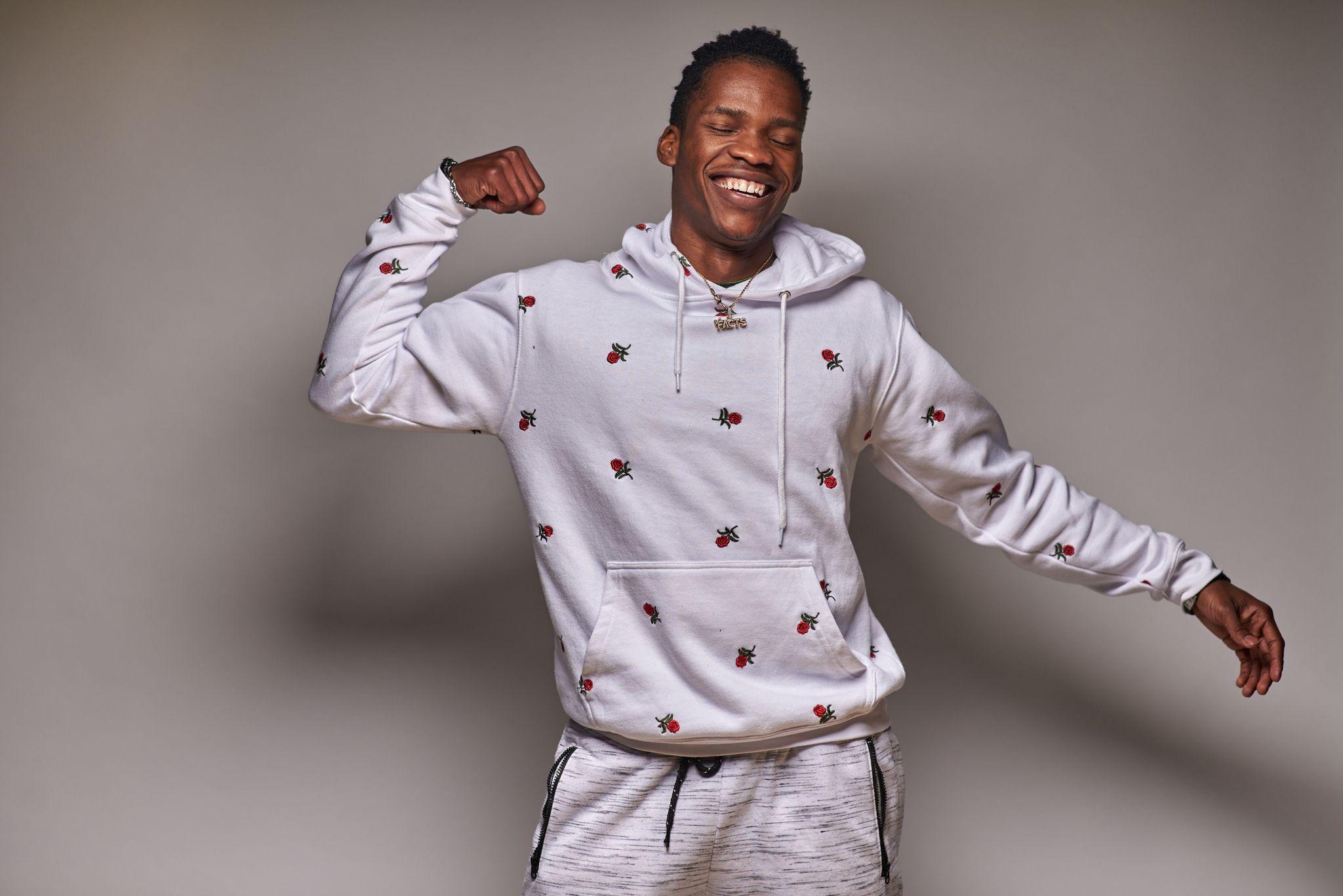 Man in a patterned white hoodie flexing one arm against a gray studio backdrop — Commercial photo studio, Austin Man in a patterned white hoodie flexing one arm against a gray studio backdrop