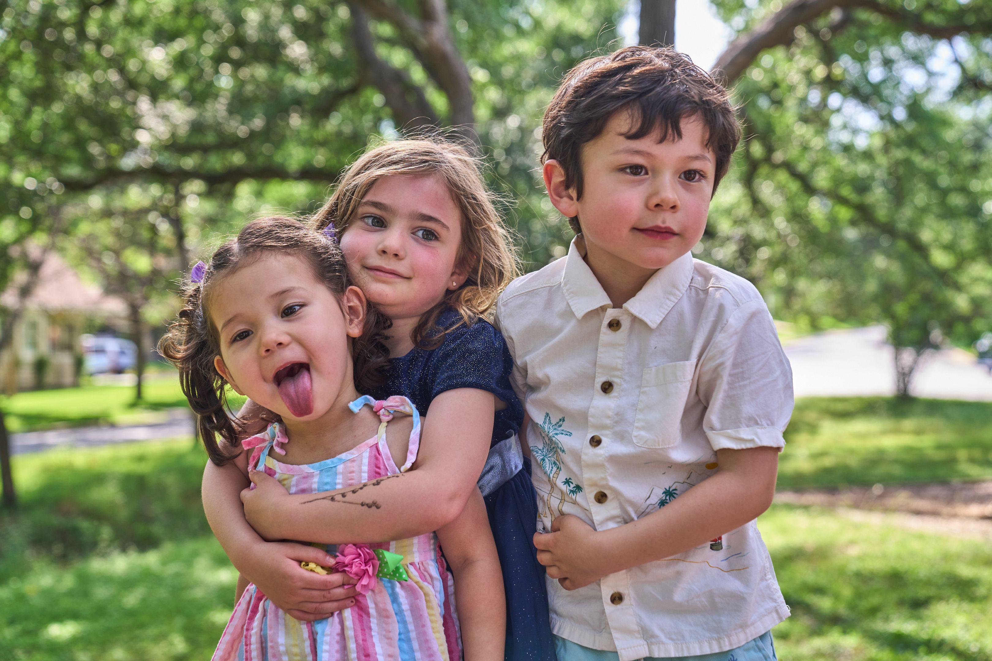 Three siblings hugging, the smallest sticking her tongue out at camera — Kids Portraits photography, Austin Three siblings hugging, the smallest sticking her tongue out at camera.