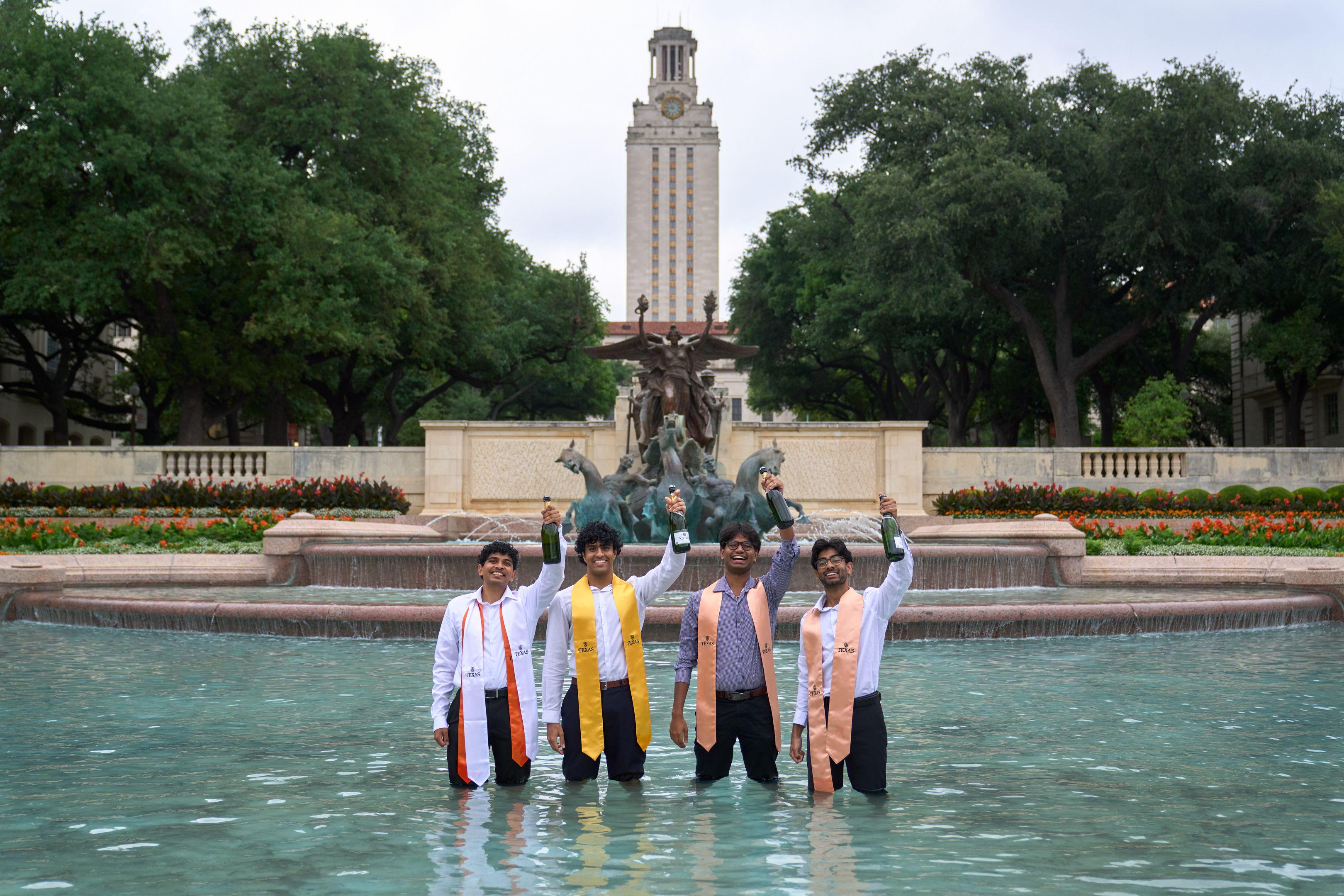 Four graduates in graduation stoles standing knee-deep in the UT Austin fountain — Graduation & Prom photography, Austin Four graduates in graduation stoles standing knee-deep in the UT Austin fountain.