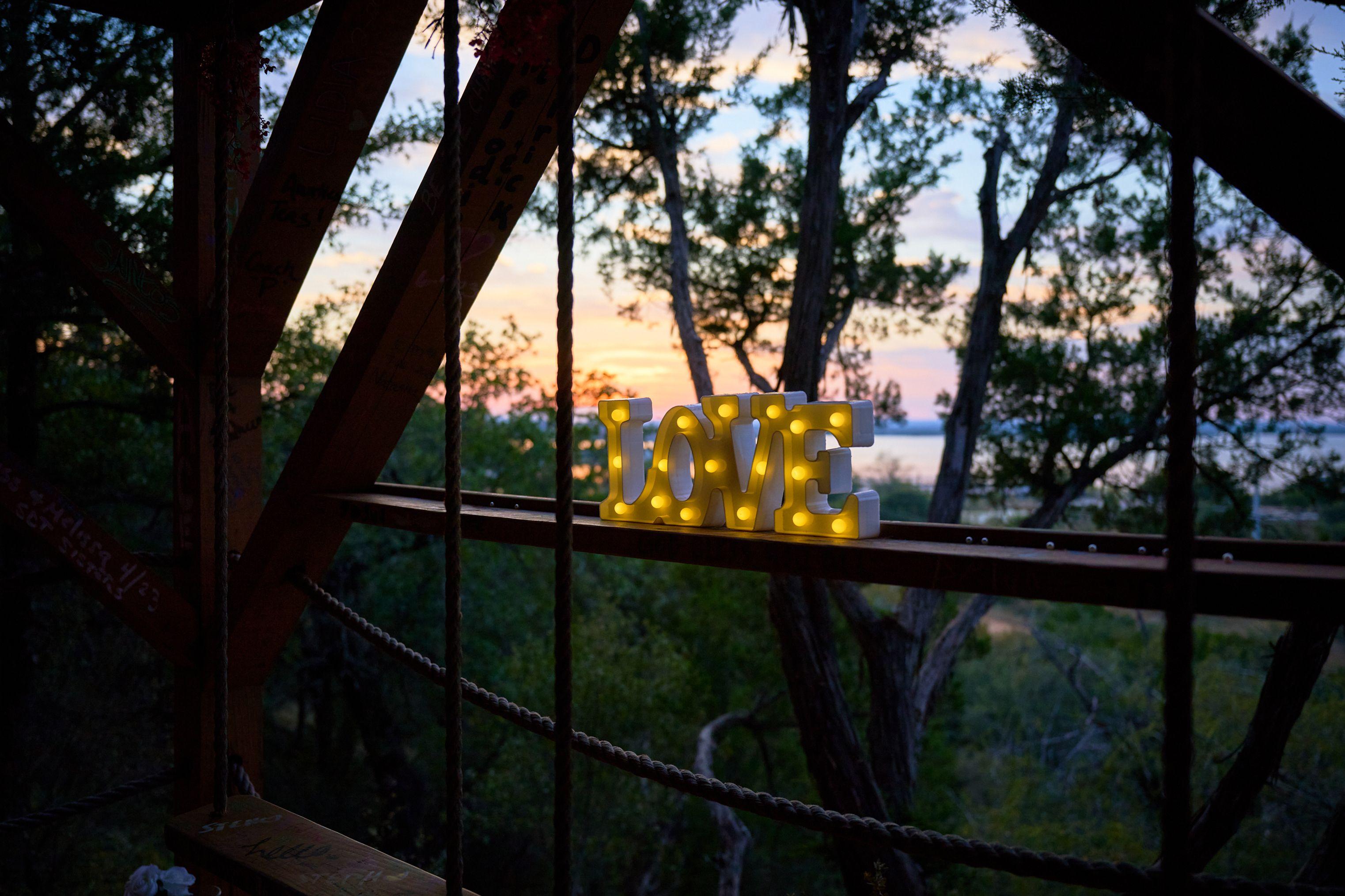 Illuminated LOVE marquee sign glowing against trees at dusk — Engagement & Proposals photography, Austin An illuminated LOVE marquee sign glowing against trees at dusk.