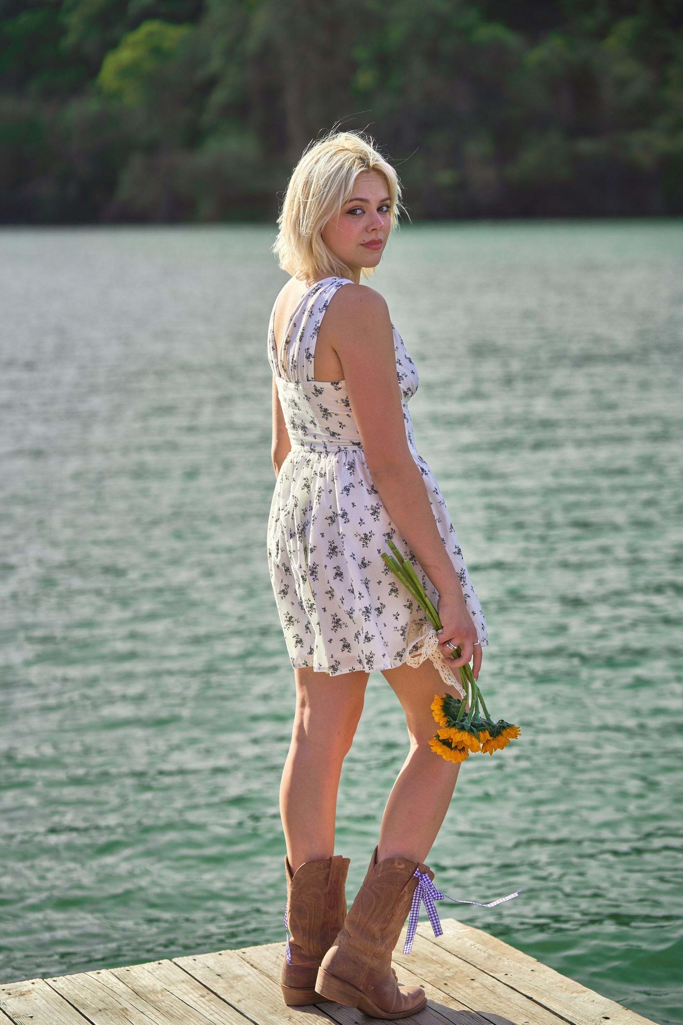 Woman in a floral dress standing on a dock by the water, holding flowers — Commons Ford Ranch photography, Austin A woman in a floral dress standing on a dock by the water, holding flowers.