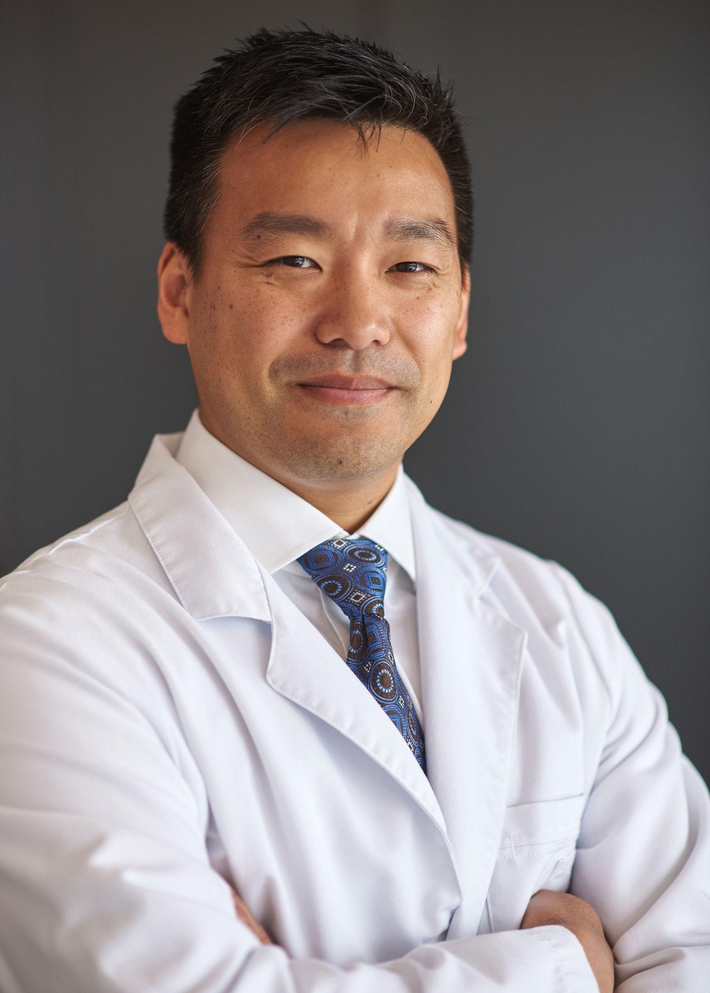 Doctor in a white coat and tie against a gray studio background — Headshot photography, Austin A doctor in a white coat and tie against a gray studio background.