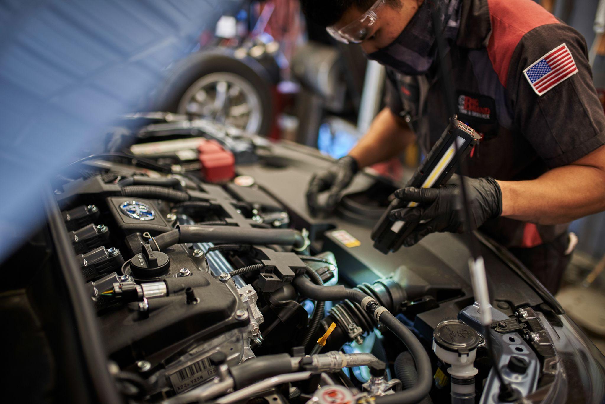 Technician leaning into an open engine bay under work lights in an auto shop — Industrial photography, Austin Technician leaning into an open engine bay under work lights in an auto shop