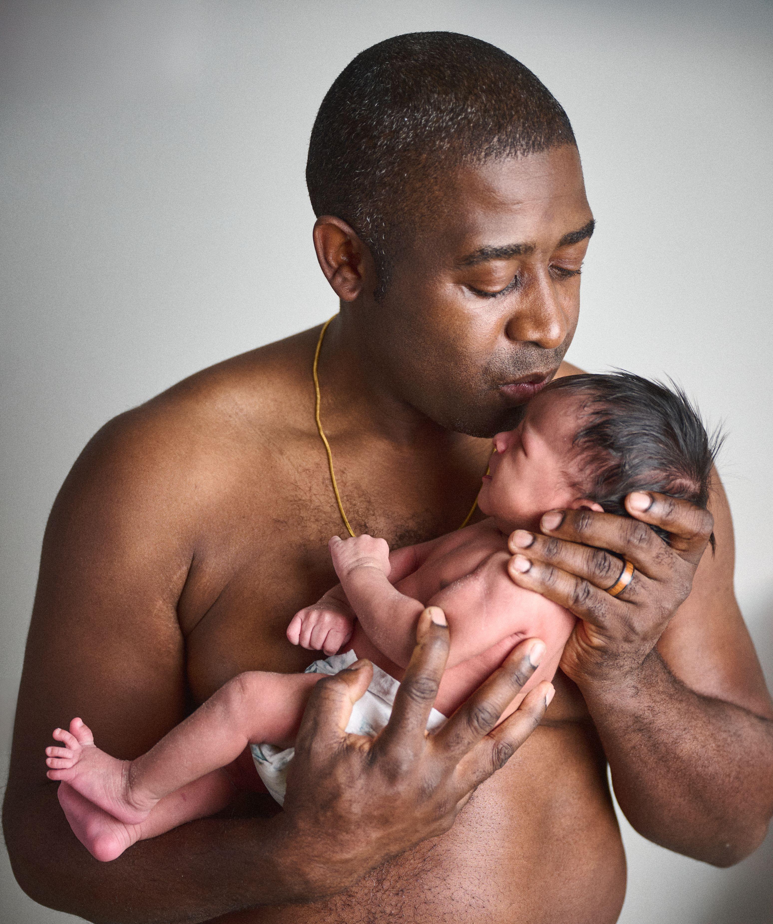 Father kissing his newborn baby, the child held against his chest on a plain backdrop — Mobile photo studio, Austin A father kissing his newborn baby, the child held against his chest on a plain backdrop