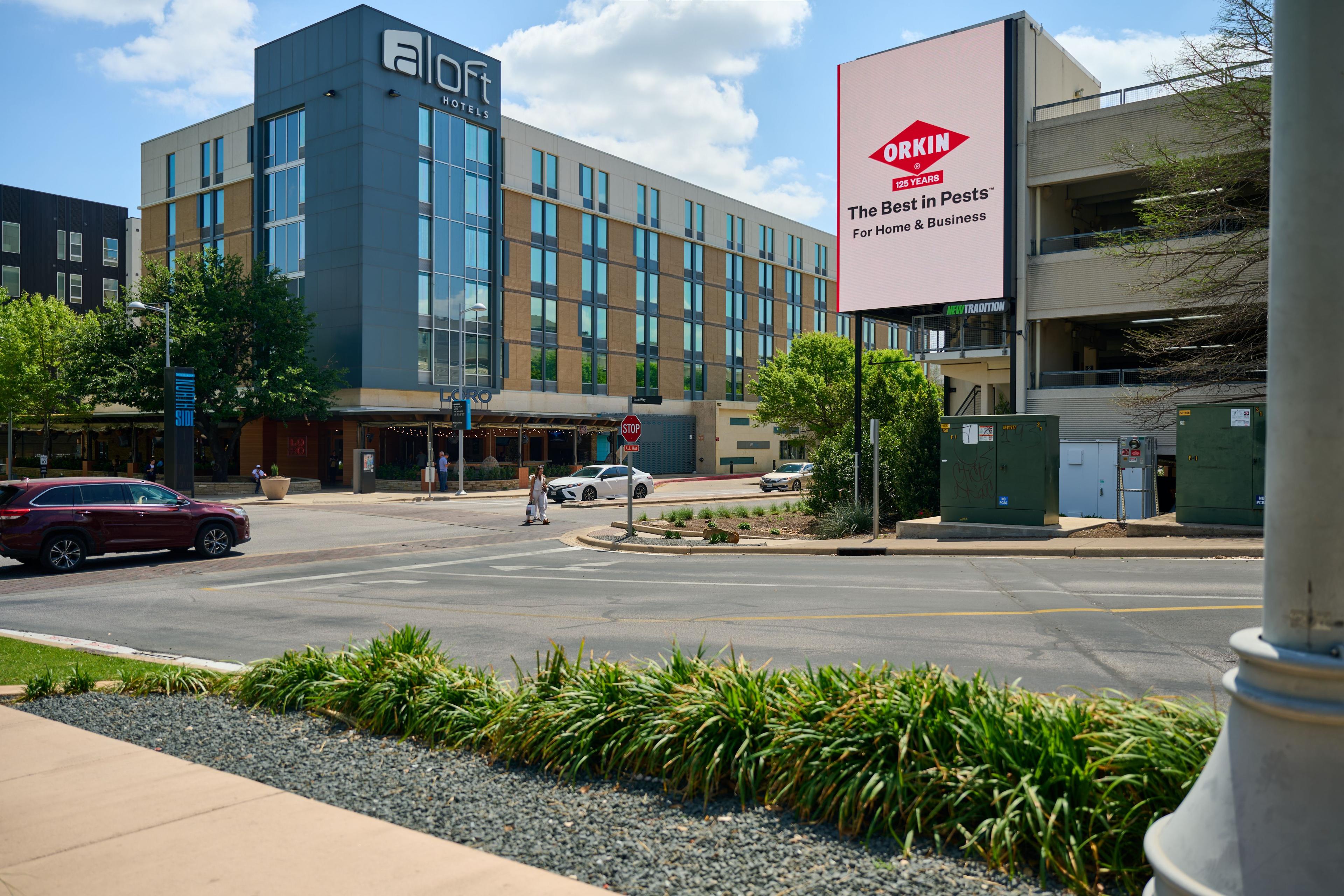 Orkin billboard mounted on the side of the Aloft hotel building in daylight — Outdoor media photography, Austin An Orkin billboard mounted on the side of the Aloft hotel building in daylight.