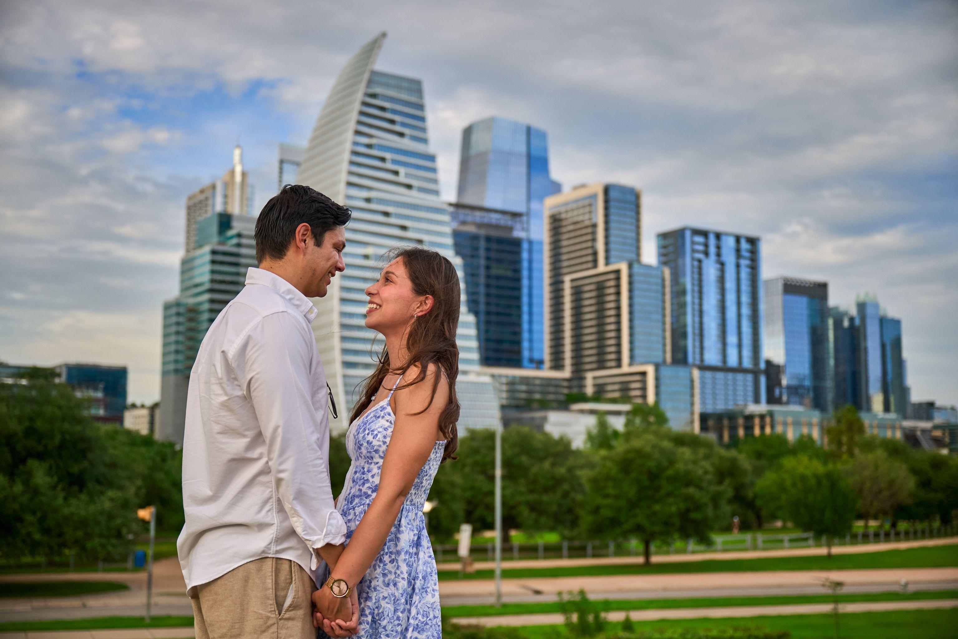 Engaged couple facing each other, hands joined, with the Austin skyline behind them — Butler Metro Park photography, Austin An engaged couple facing each other, hands joined, with the Austin skyline behind them.