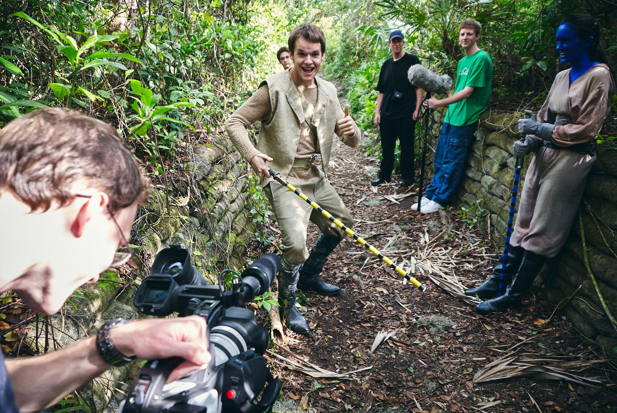 Actor in period costume holding a rope on a wooded trail while crew with a camera follow — Production behind-the-scenes, Austin Actor in period costume holding a rope on a wooded trail while crew with a camera follow behind