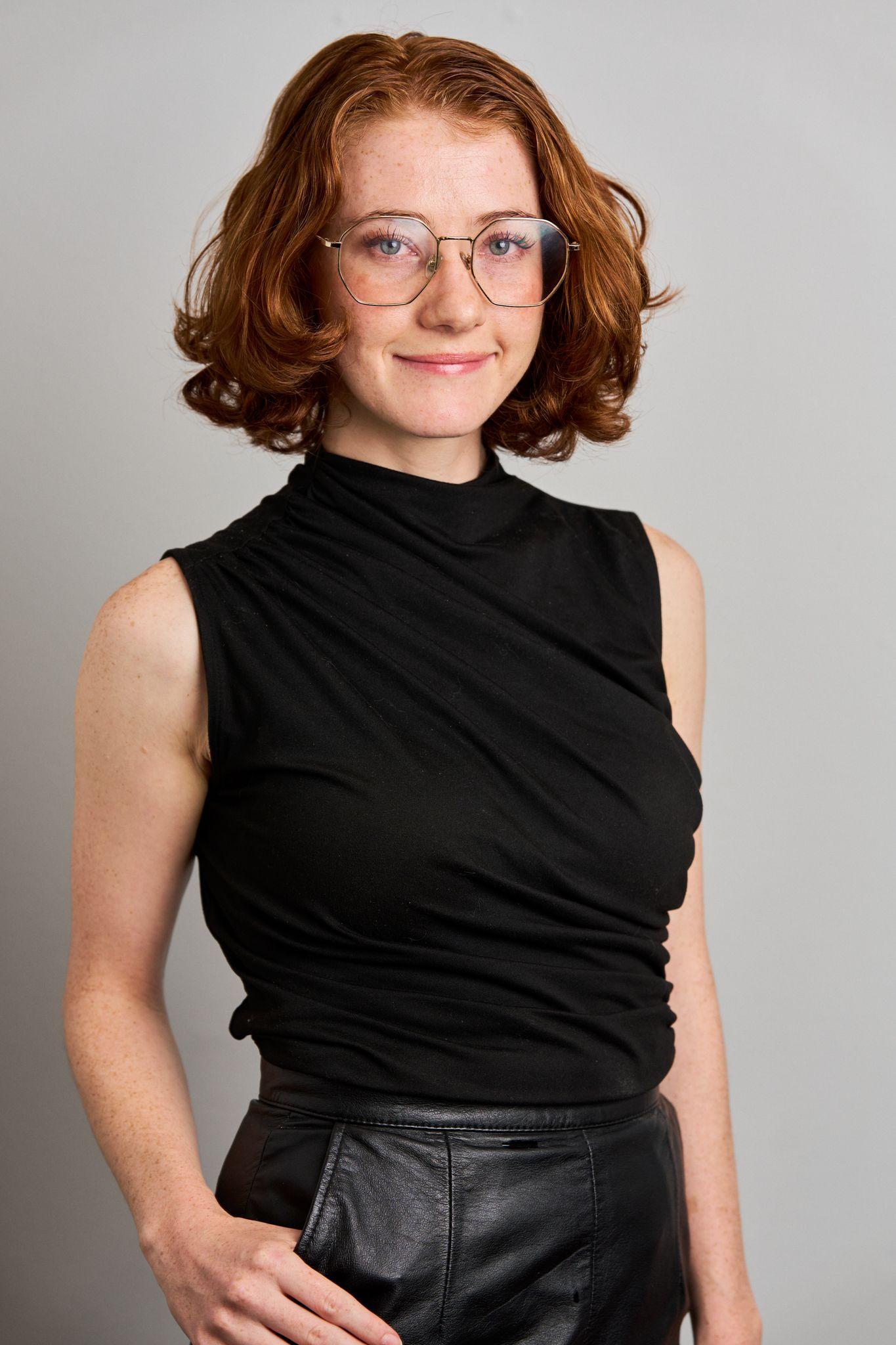 Woman with short red hair in a black sleeveless top, photographed — Business headshots, Austin A woman with short red hair in a black sleeveless top, photographed against a plain gray studio background