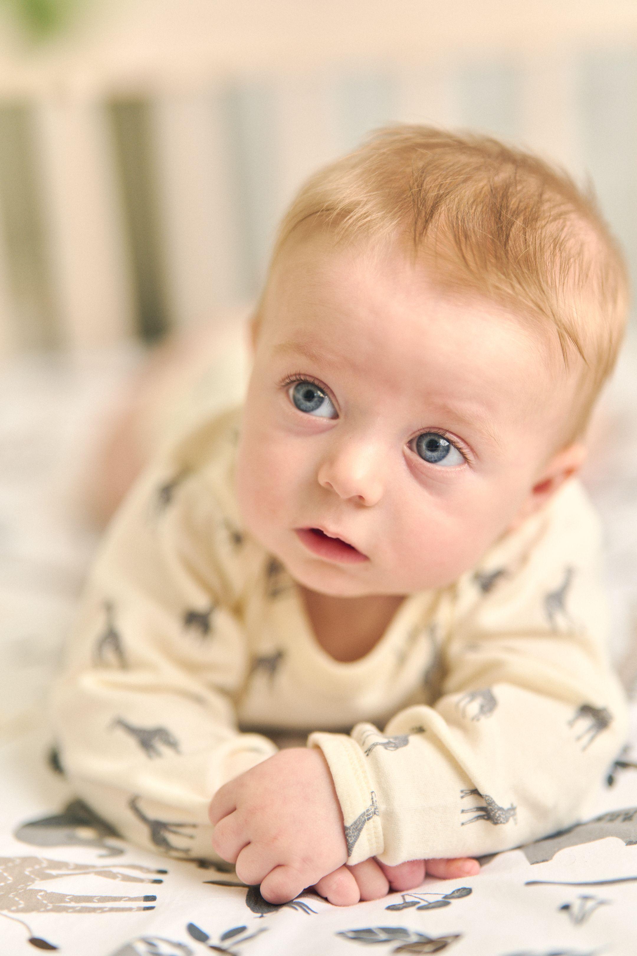 Baby in a giraffe-print sleepsuit propped on his front, looking up — Newborn photography, Austin A baby in a giraffe-print sleepsuit propped on his front, looking up.