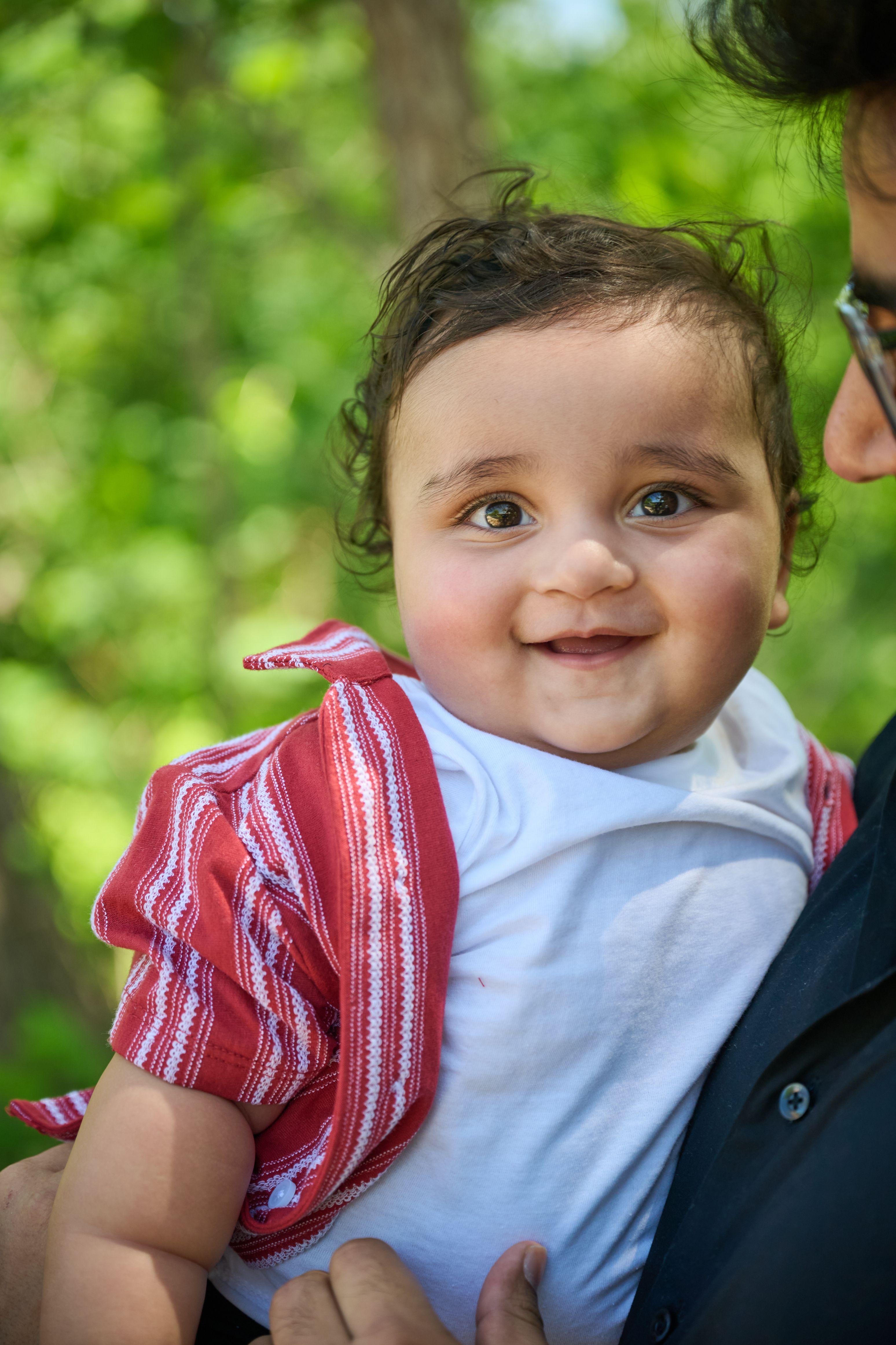 Smiling baby in a red striped shirt held up against the green trees beside the boardwalk — Austin Boardwalk photography, Austin A smiling baby in a red striped shirt held up against the green trees beside the boardwalk