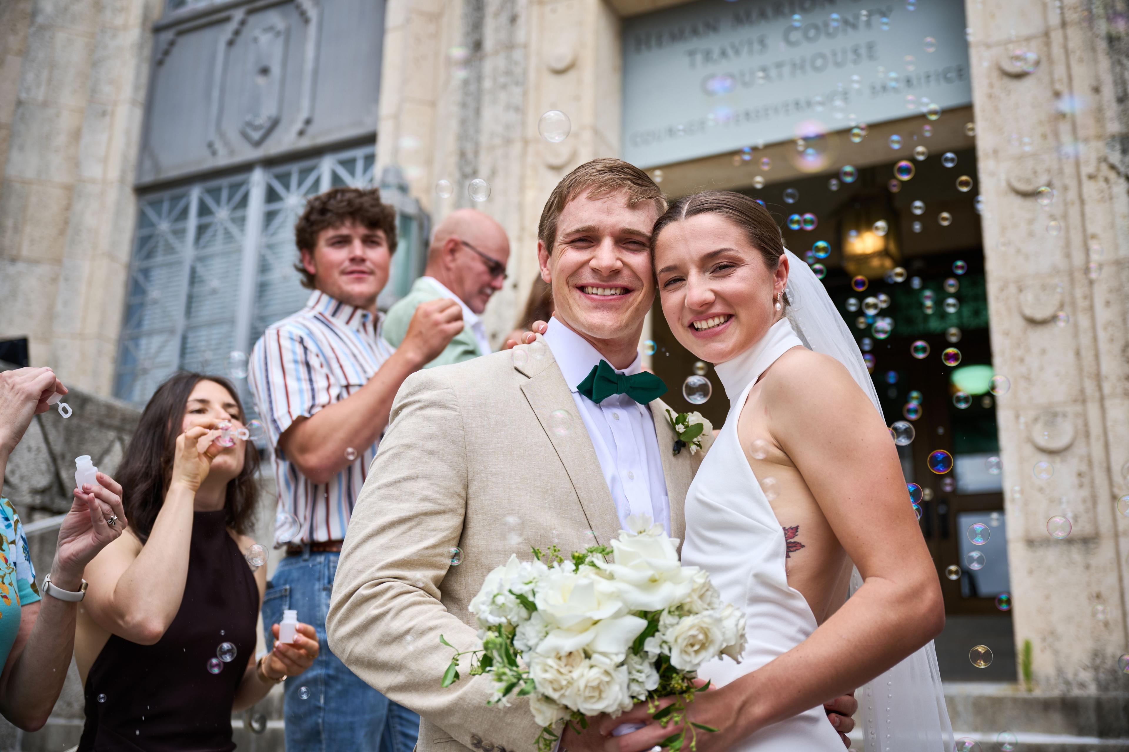 Couple laughing with friends outside the courthouse, bubbles drifting past — Weddings photography, Austin A couple laughing with friends outside the courthouse, bubbles drifting past.