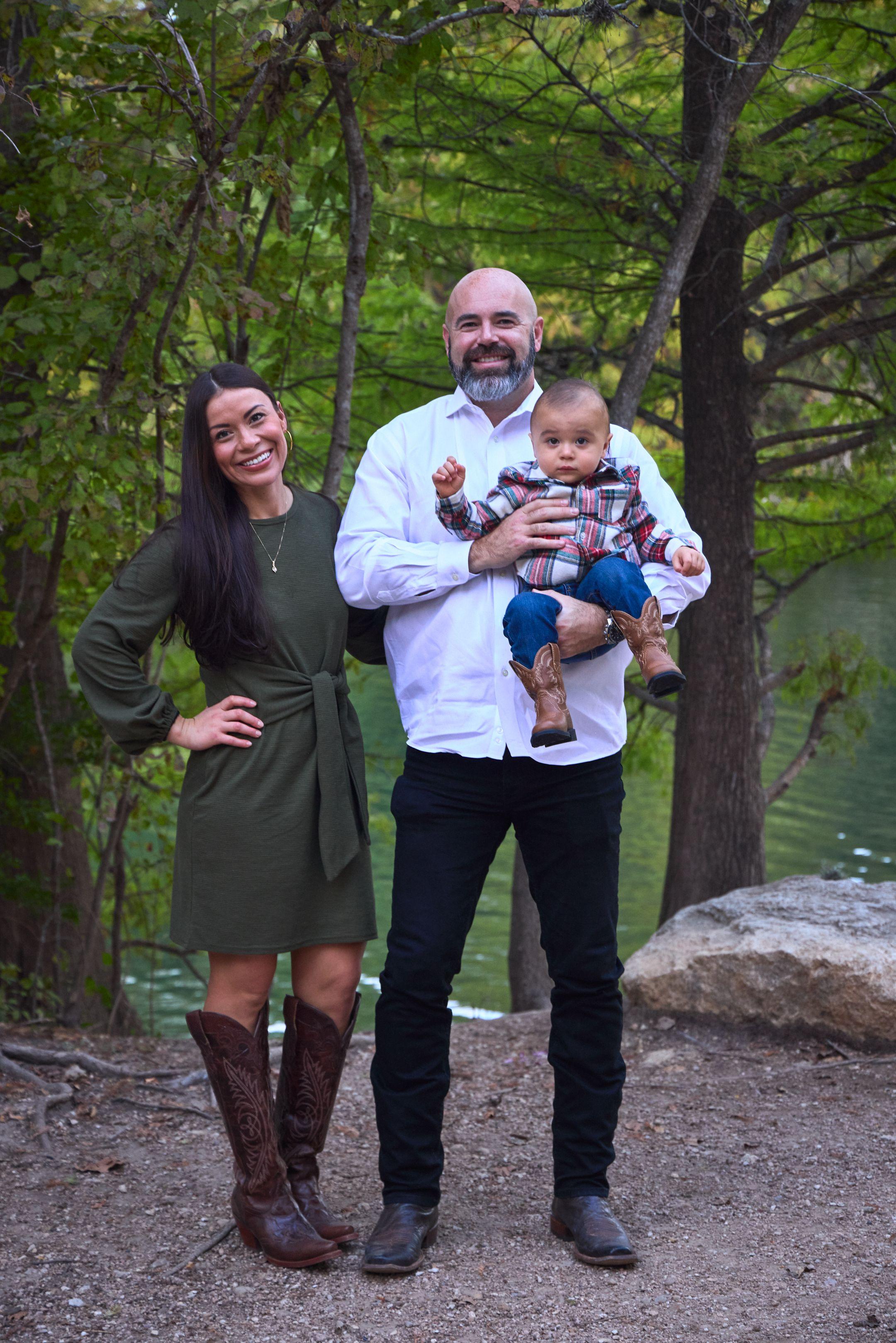 Mother, father and baby standing among the trees at Red Bud Isle with the water behind them — Red Bud Isle photography, Austin A mother, father and baby standing among the trees at Red Bud Isle with the water behind them