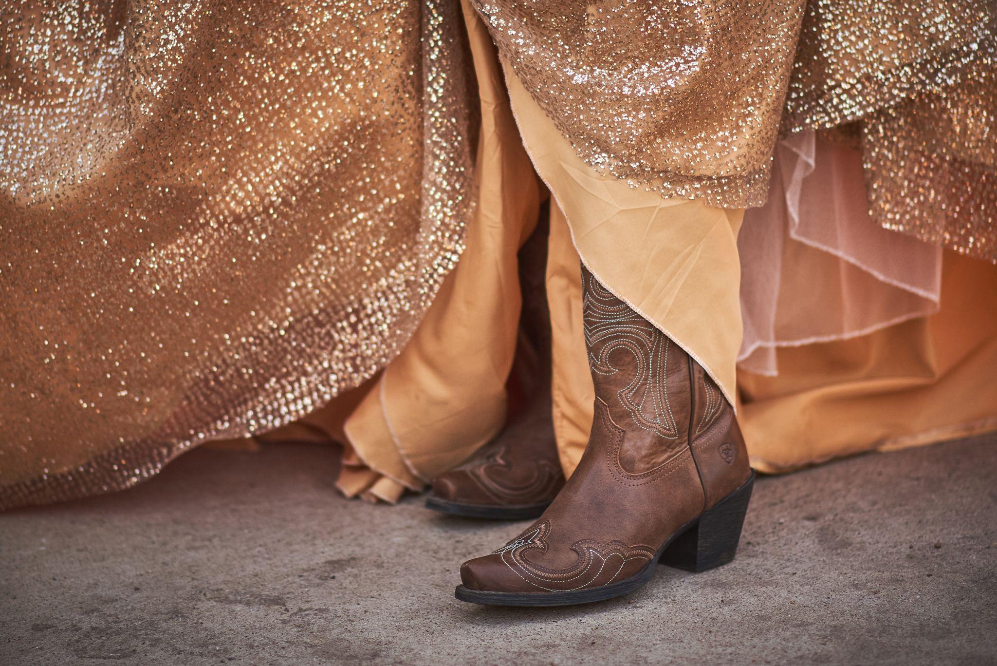 Close crop of brown embroidered cowboy boots beneath a gold sequinned skirt on pavement — E-commerce & apparel photography, Austin Close crop of brown embroidered cowboy boots beneath a gold sequinned skirt on pavement