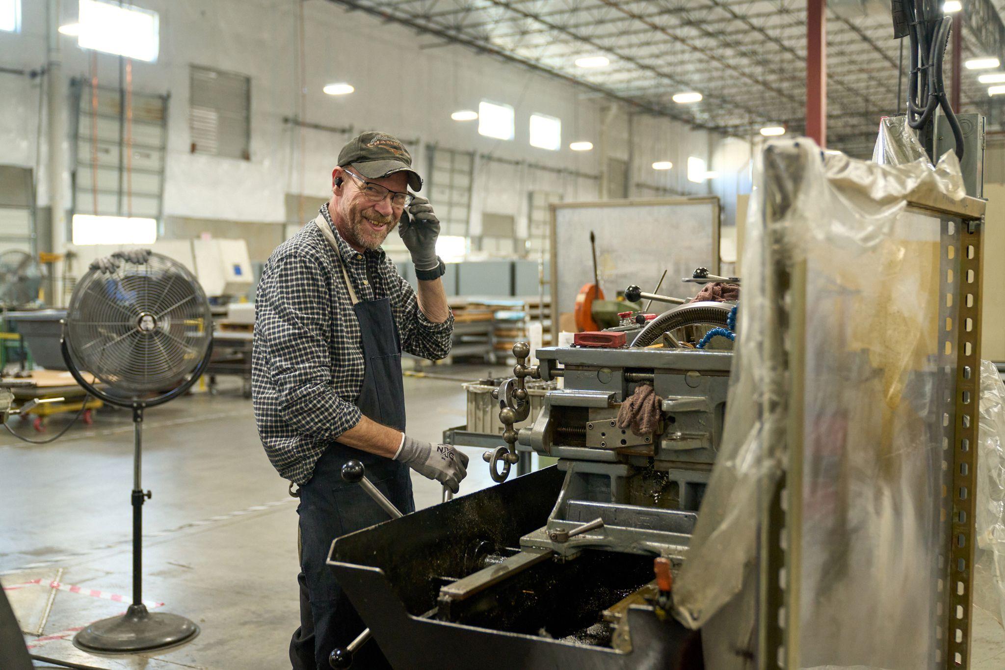 Machinist in a plaid shirt clearing metal shavings from a lathe bed in a workshop — Industrial photography, Austin Machinist in a plaid shirt clearing metal shavings from a lathe bed in a workshop