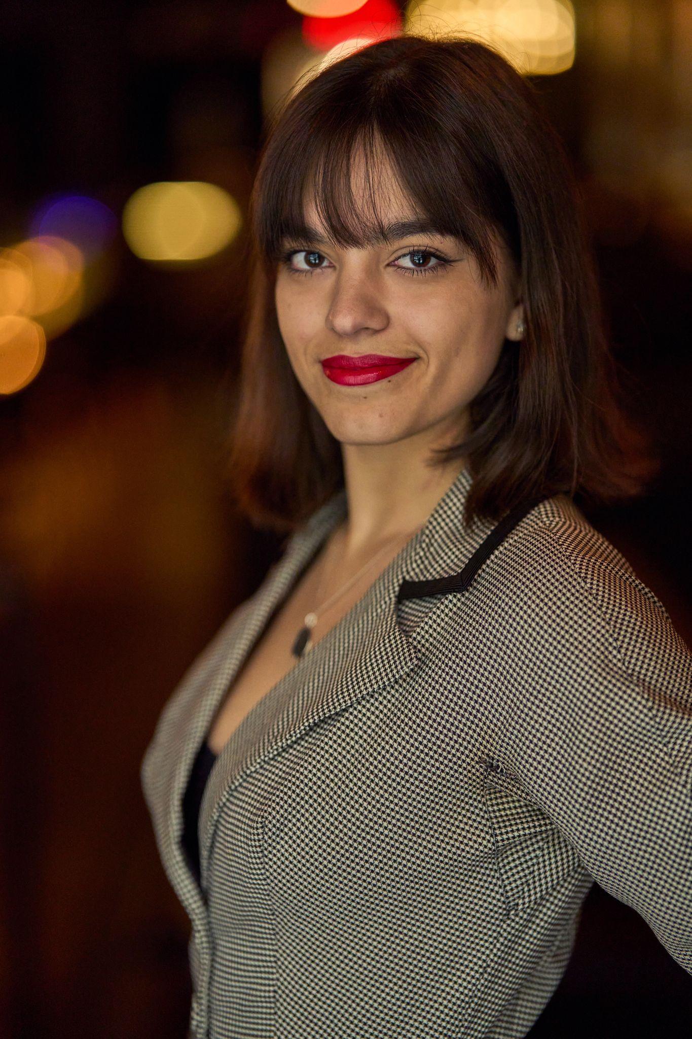 Woman in a checked blazer photographed at night against city bokeh — Headshot photography, Austin A woman in a checked blazer photographed at night against city bokeh.