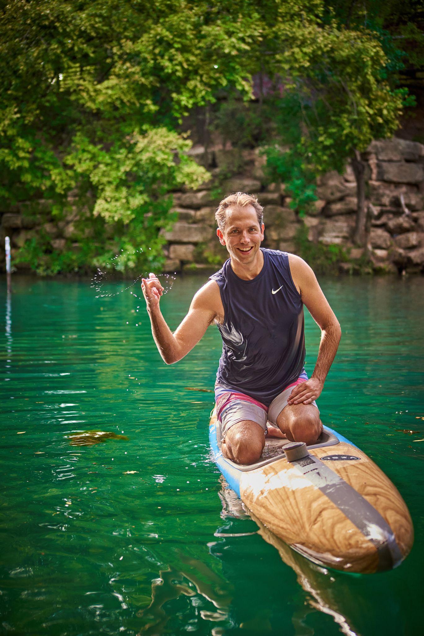 Paddleboarder kneeling on a board in green spring-fed water — Portrait photography, Austin A paddleboarder kneeling on a board in green spring-fed water.
