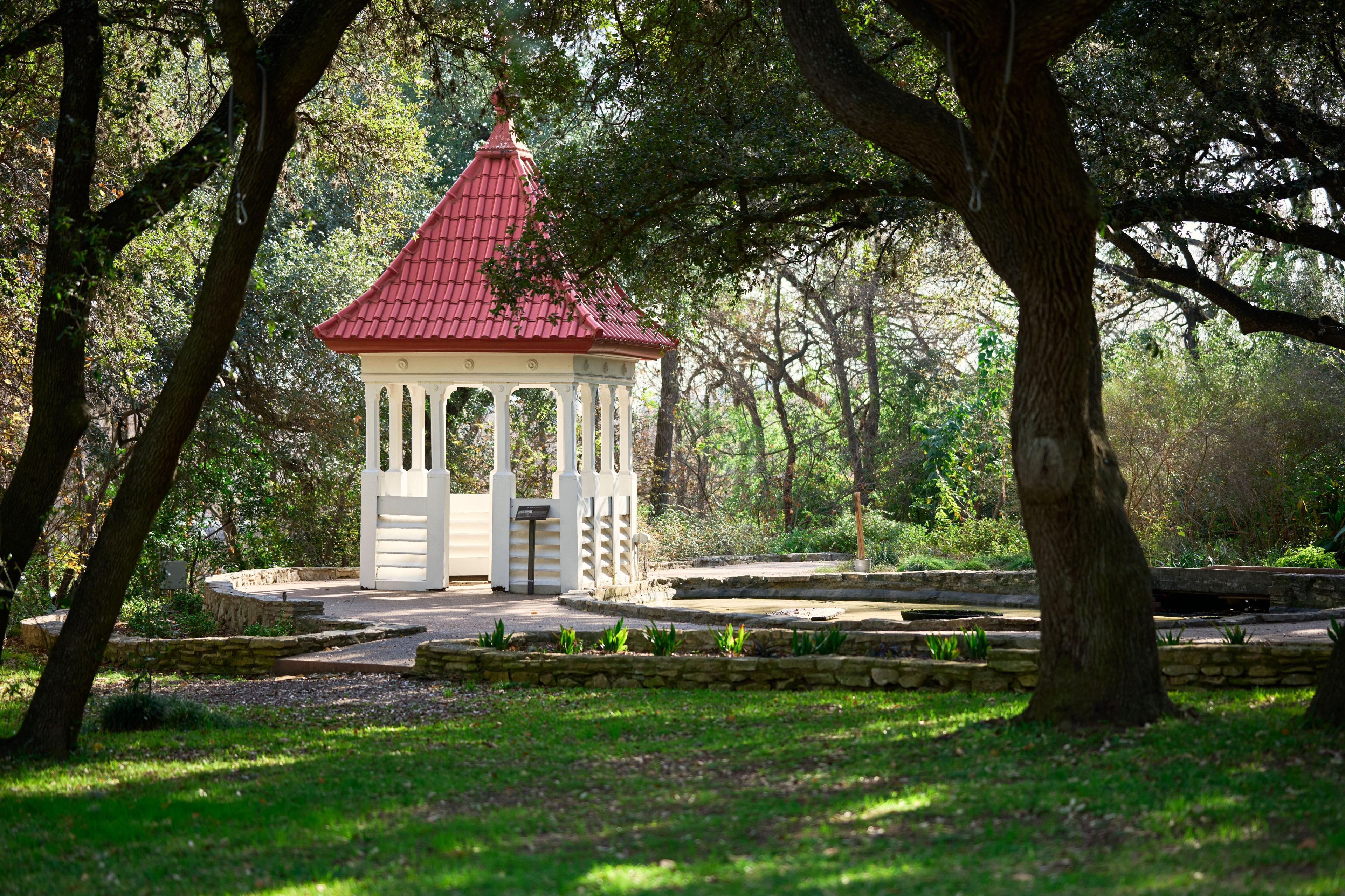 White gazebo with its red roof standing empty under live oaks at Zilker Botanical Garden — Zilker Botanical Gardens photography, Austin The white gazebo with its red roof standing empty under live oaks at Zilker Botanical Garden
