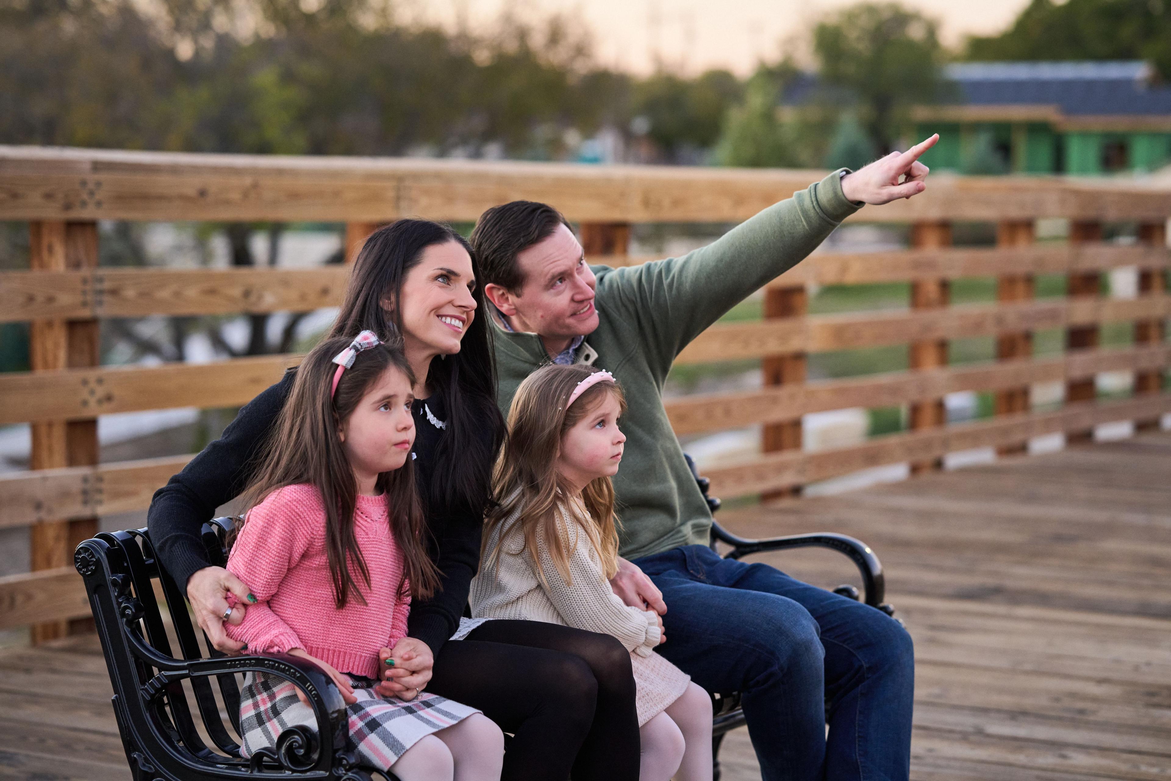 Family sitting on a bench by the rail fence at Chisholm Trail Crossing — Round Rock Chisholm Trail Crossing photography, Austin A family sitting on a bench by the rail fence at Chisholm Trail Crossing, the father pointing off toward the creek
