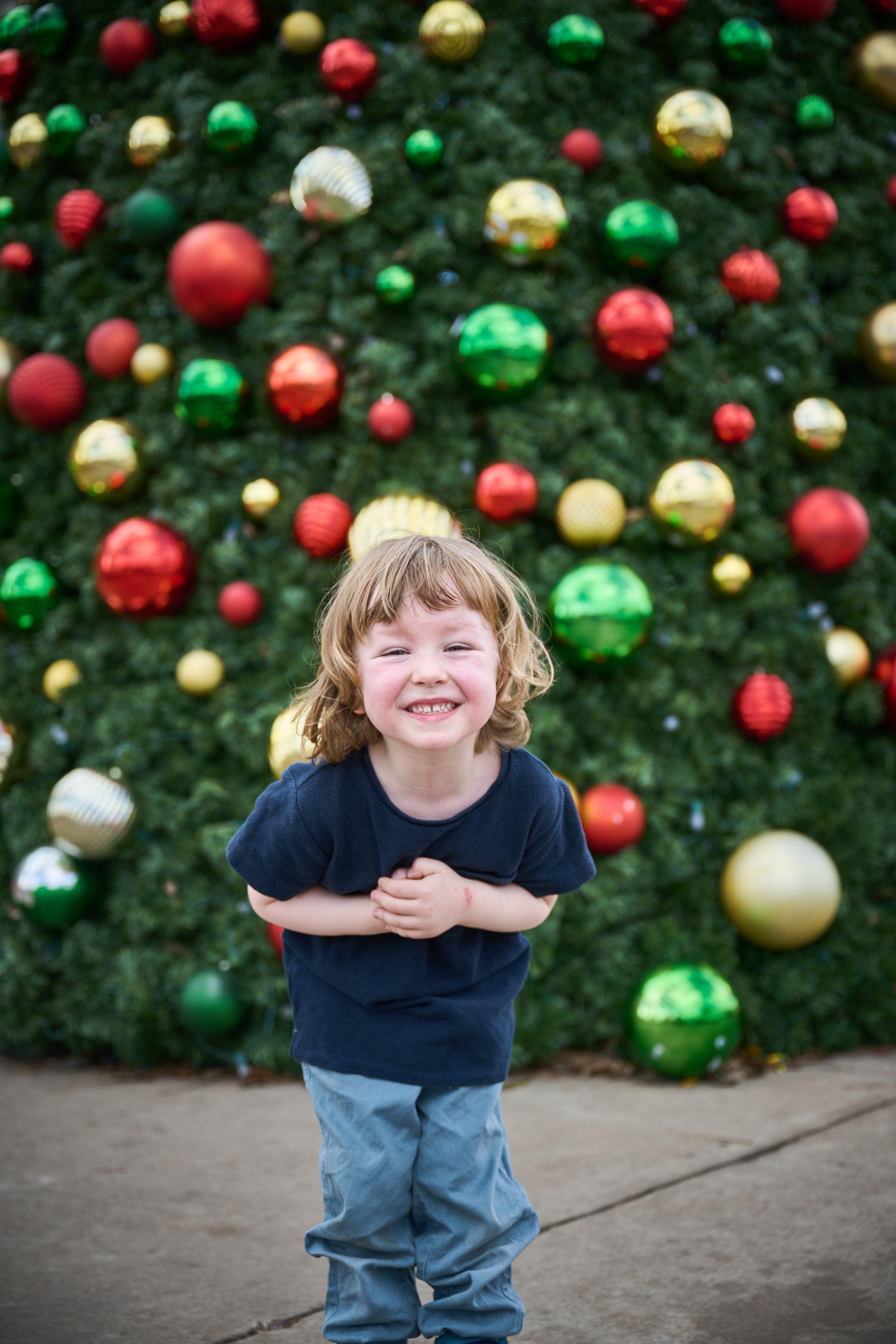 Small boy laughing in front of a wall of oversized red, green and gold baubles — Seasonal Christmas & Fall photography, Austin A small boy laughing in front of a wall of oversized red, green and gold baubles.