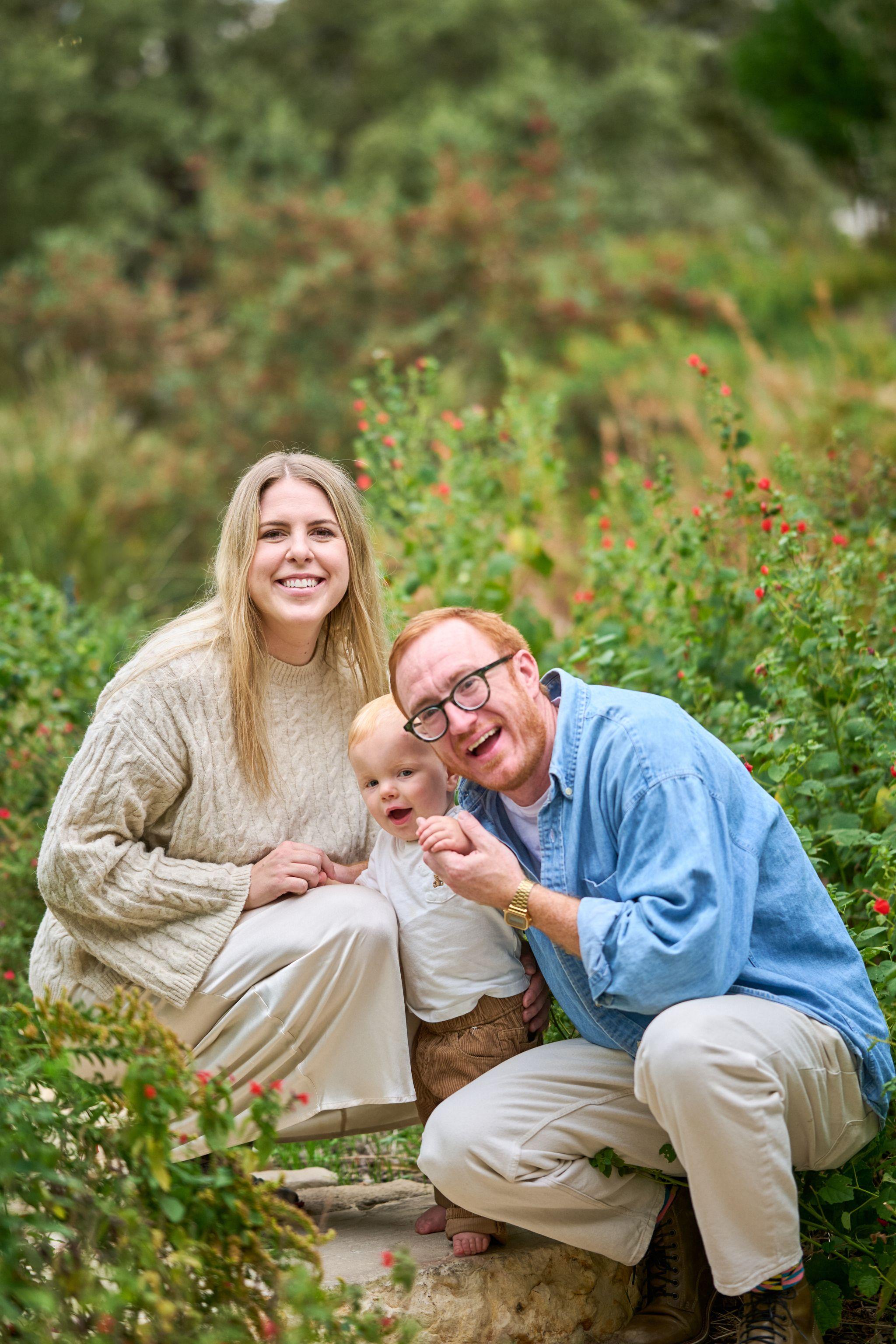 Family of three crouched together among tall native planting — Waterloo Park photography, Austin A family of three crouched together among tall native planting.