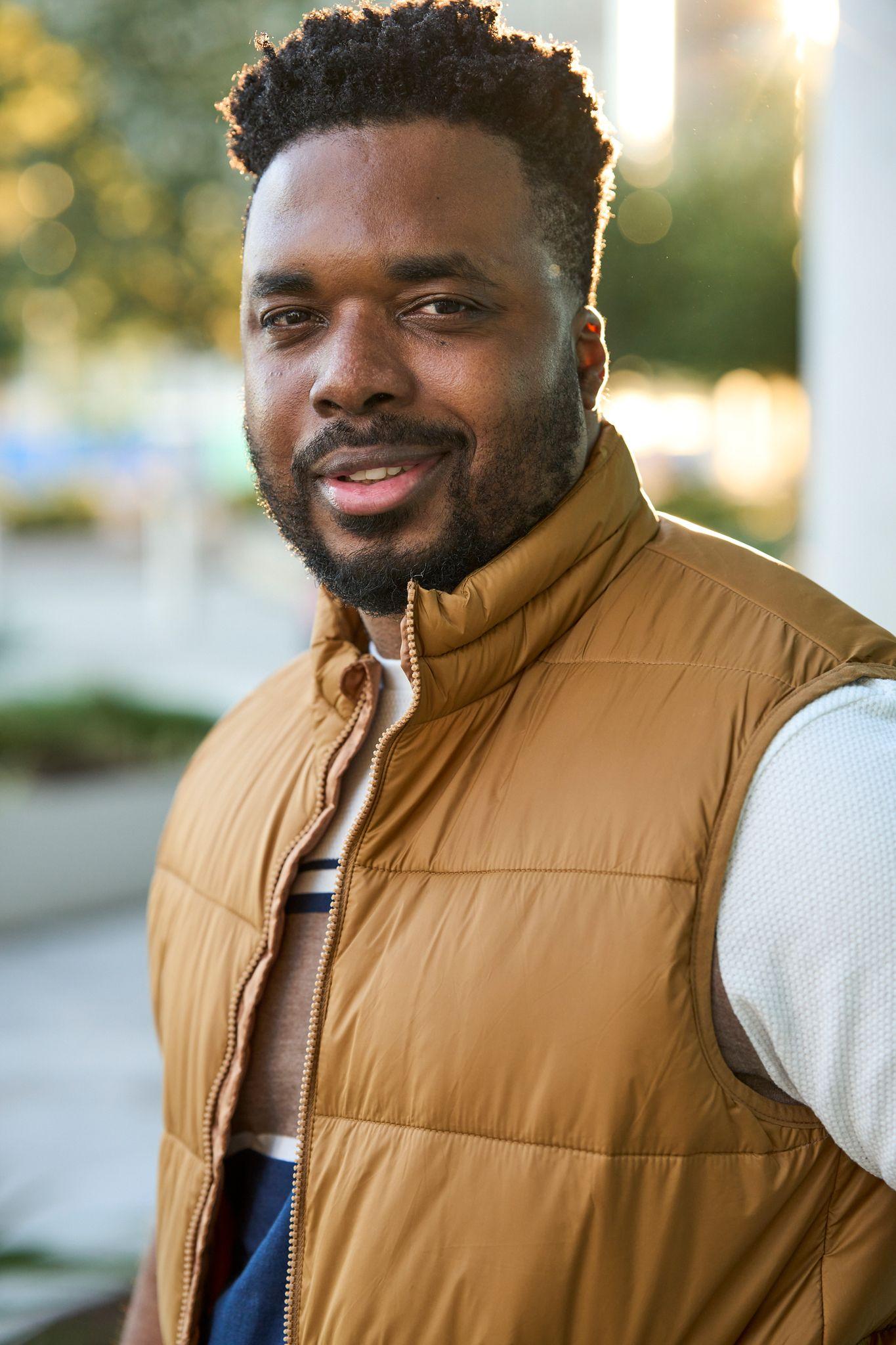 Man in a tan quilted vest photographed outdoors with a city street blurred behind him — Business headshots, Austin A man in a tan quilted vest photographed outdoors with a city street blurred behind him
