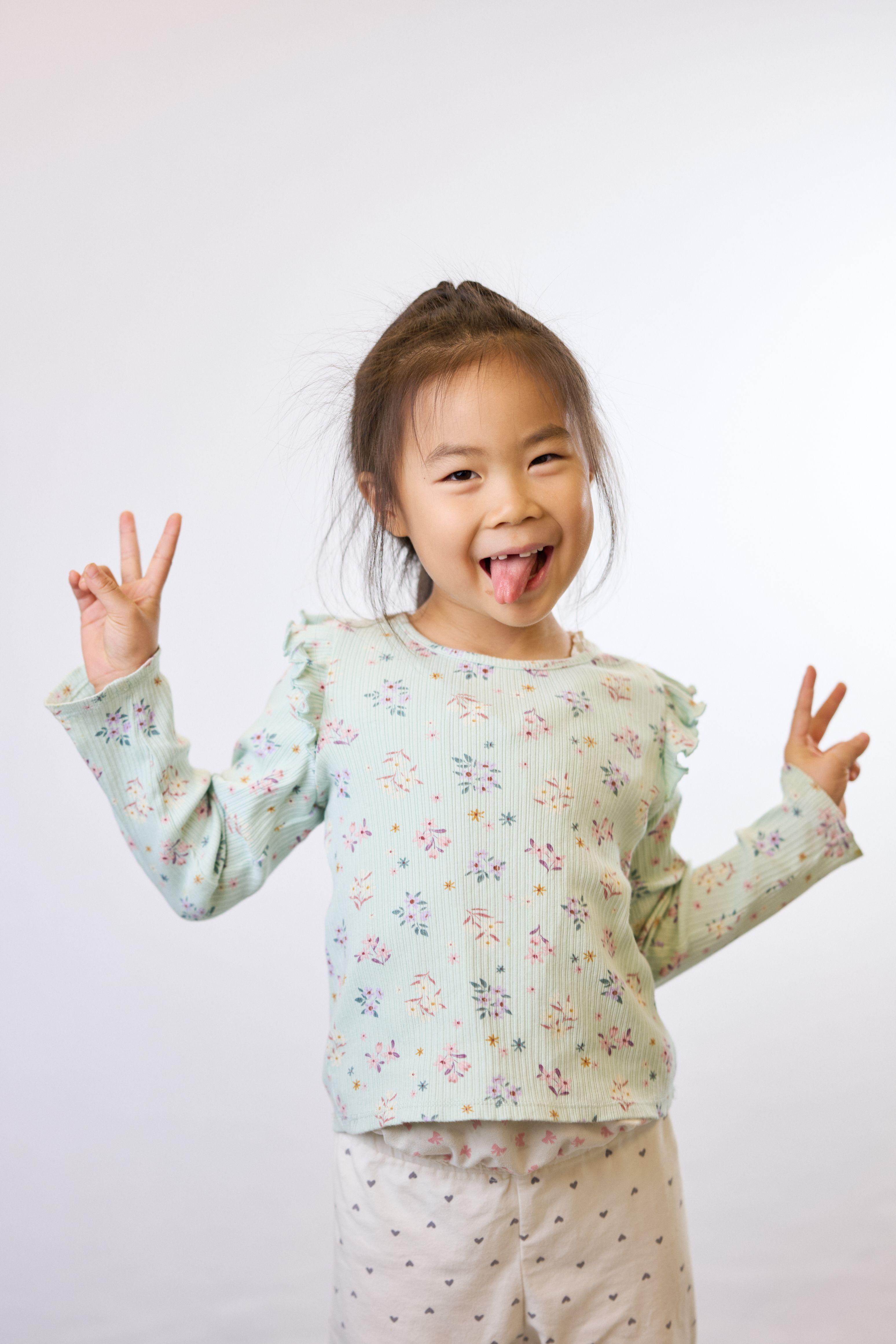 Small child in a floral top making peace signs with both hands and pulling a face — Commercial photo studio, Austin Small child in a floral top making peace signs with both hands and pulling a face on white seamless